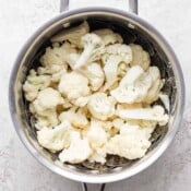 A steamer basket in a saucepan with fresh cauliflower florets inside.