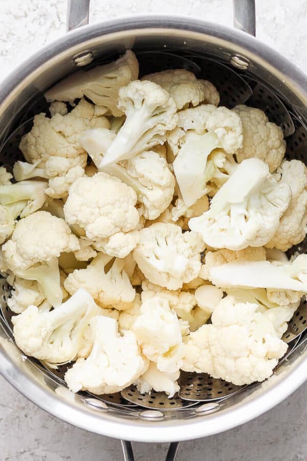 A steamer basket in a saucepan with fresh cauliflower florets inside.