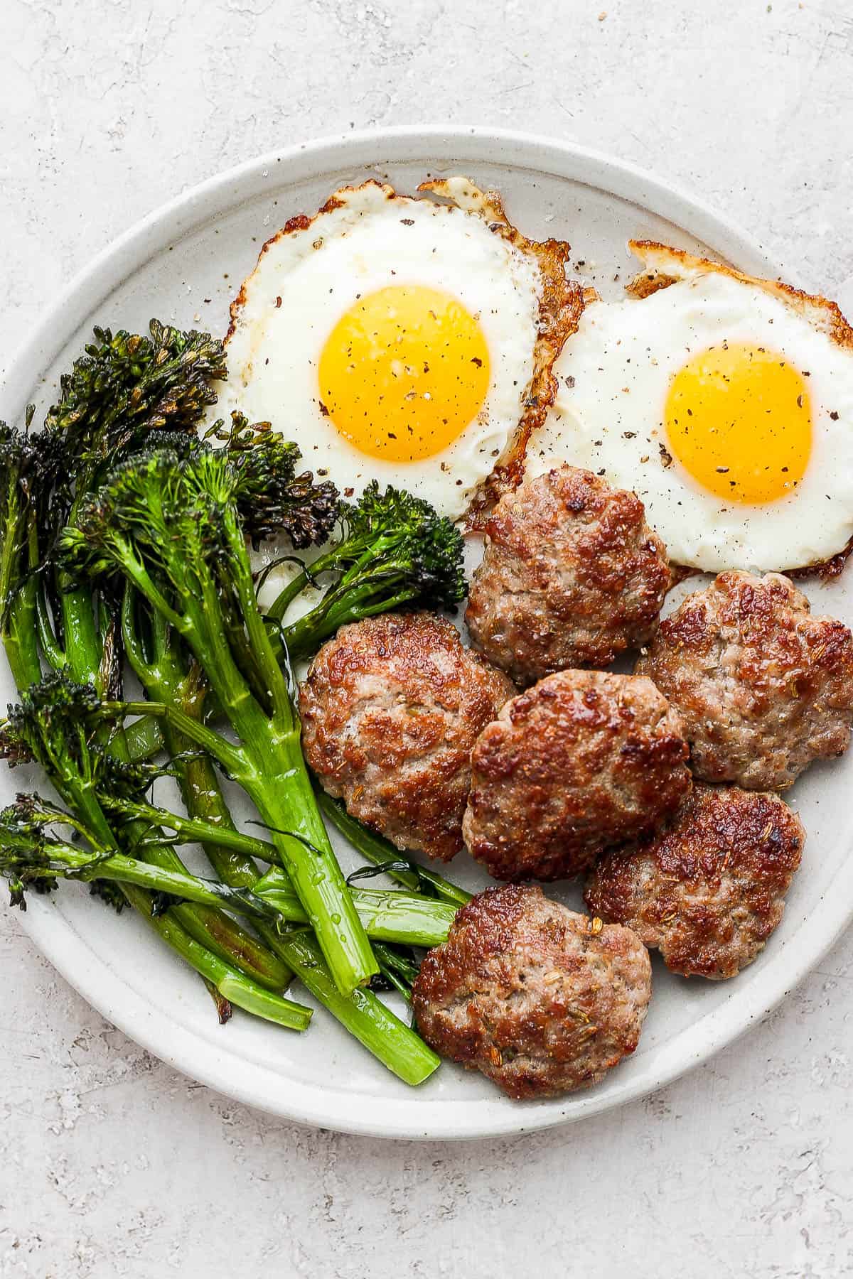 Sausage on a plate with eggs and broccolini.