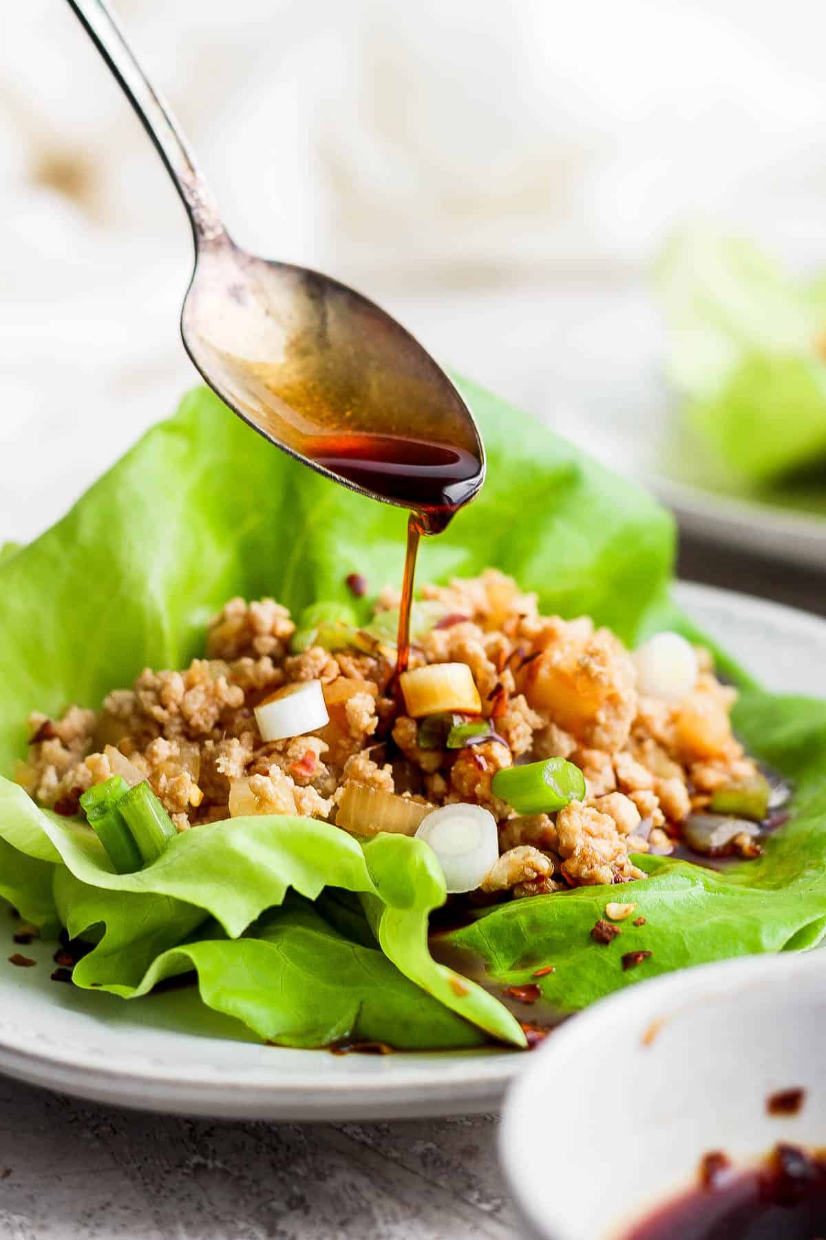 A spoon pouring more sauce on top of a chicken lettuce wrap.