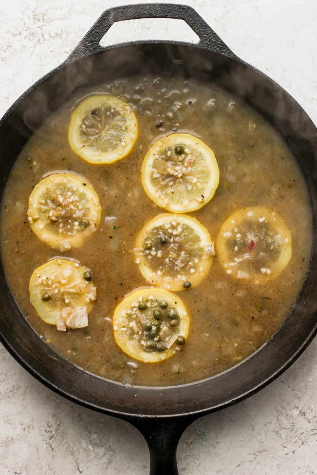 Chicken broth, white wine, lemon juice, lemon zest, lemon slices, and capers added to the pan.