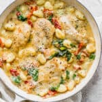 A large braising pan filled with creamy tuscan chicken with gnocchi, kale and tomatoes.