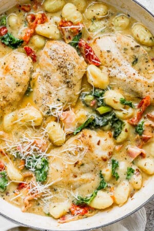 A large braising pan filled with creamy tuscan chicken with gnocchi, kale and tomatoes.