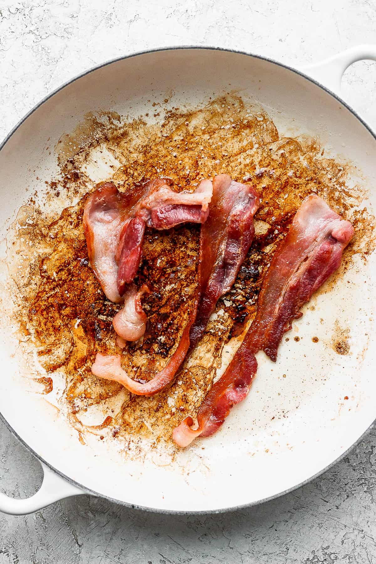 Bacon cooking in a large white skillet.