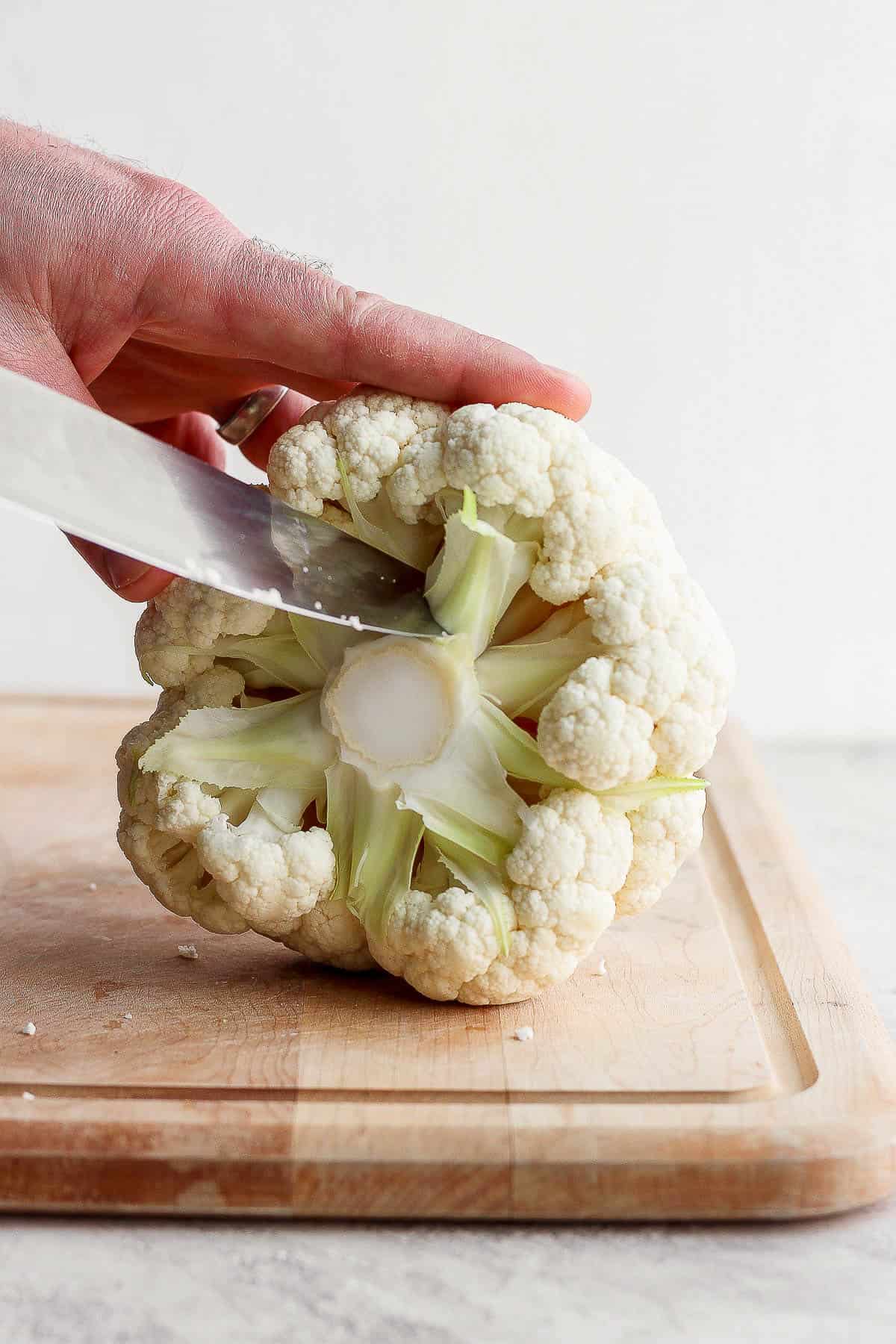 A head of cauliflower on a cutting board and the stem being removed.