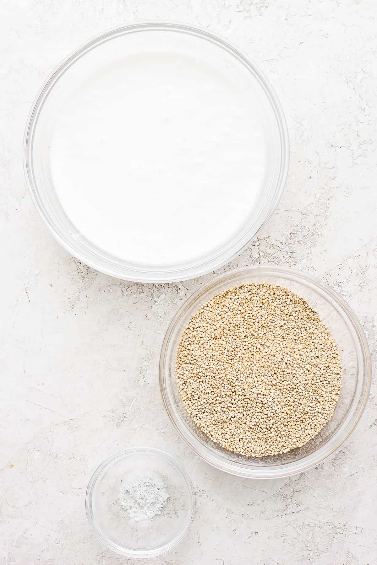 A bowl of coconut milk, a bowl of quinoa, and a small bowl of salt on a countertop. 