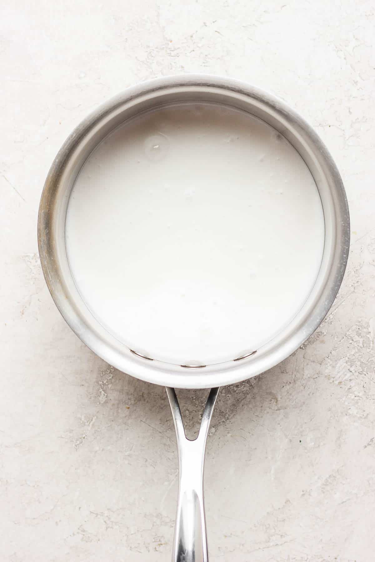 A medium sized sauce pan with coconut milk inside. 