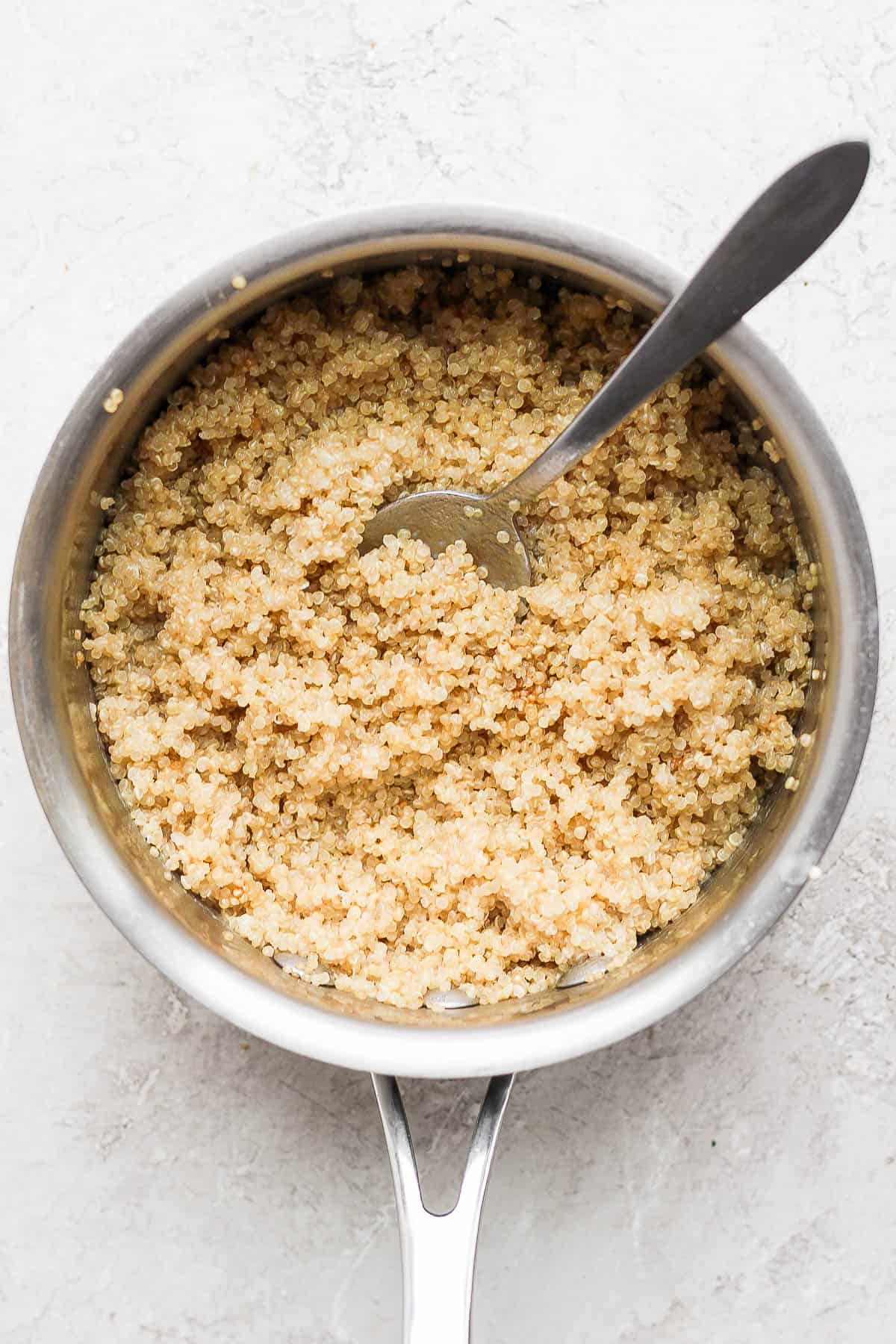 Cooked coconut quinoa in a sauce pan with a spoon stuck into the middle.