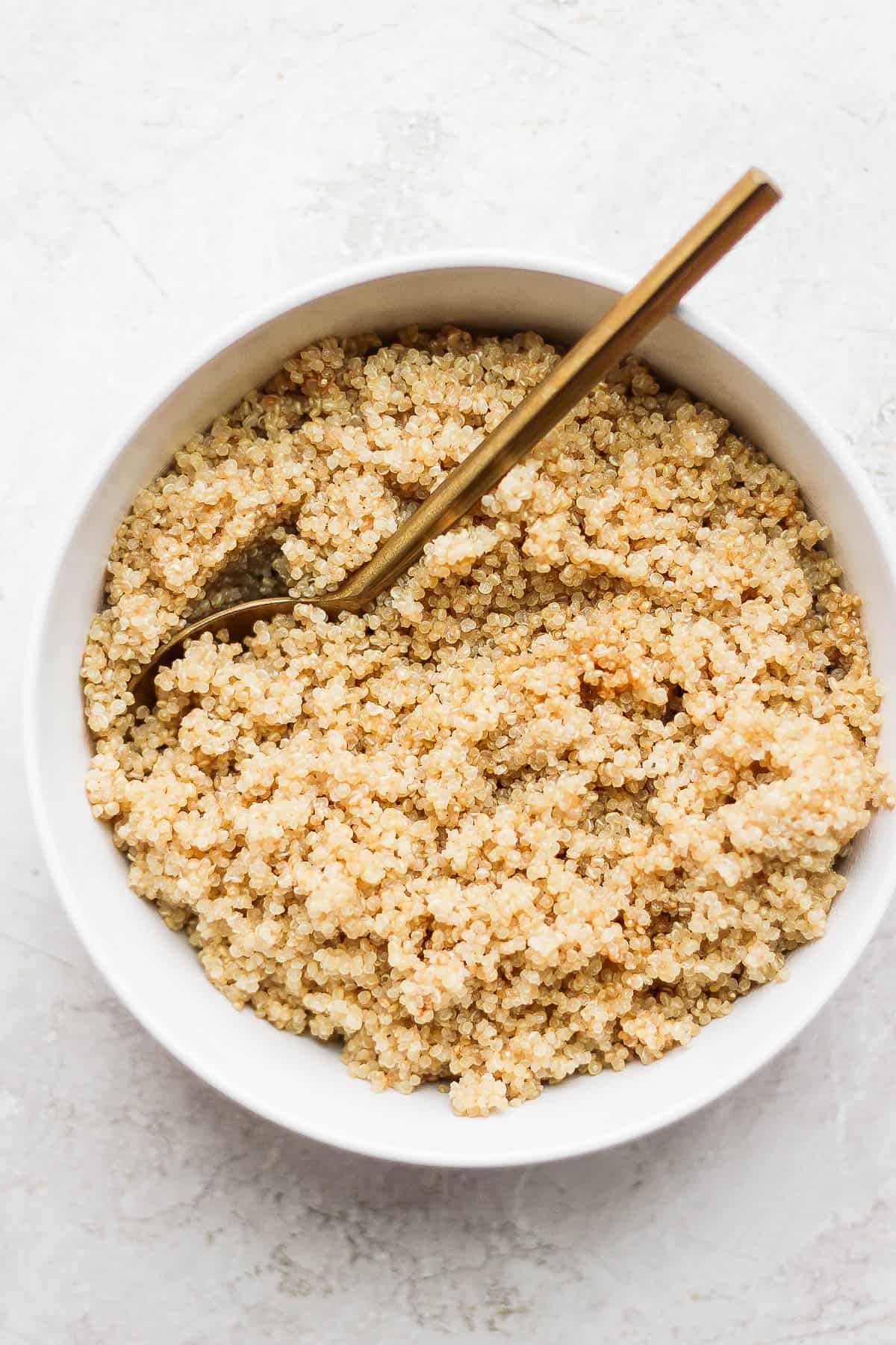 Coconut quinoa in a white bowl with a golden spoon sticking into it and leaning on the side of the bowl. 