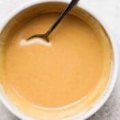 Bowl of creamy peanut sauce with spoon sticking out.