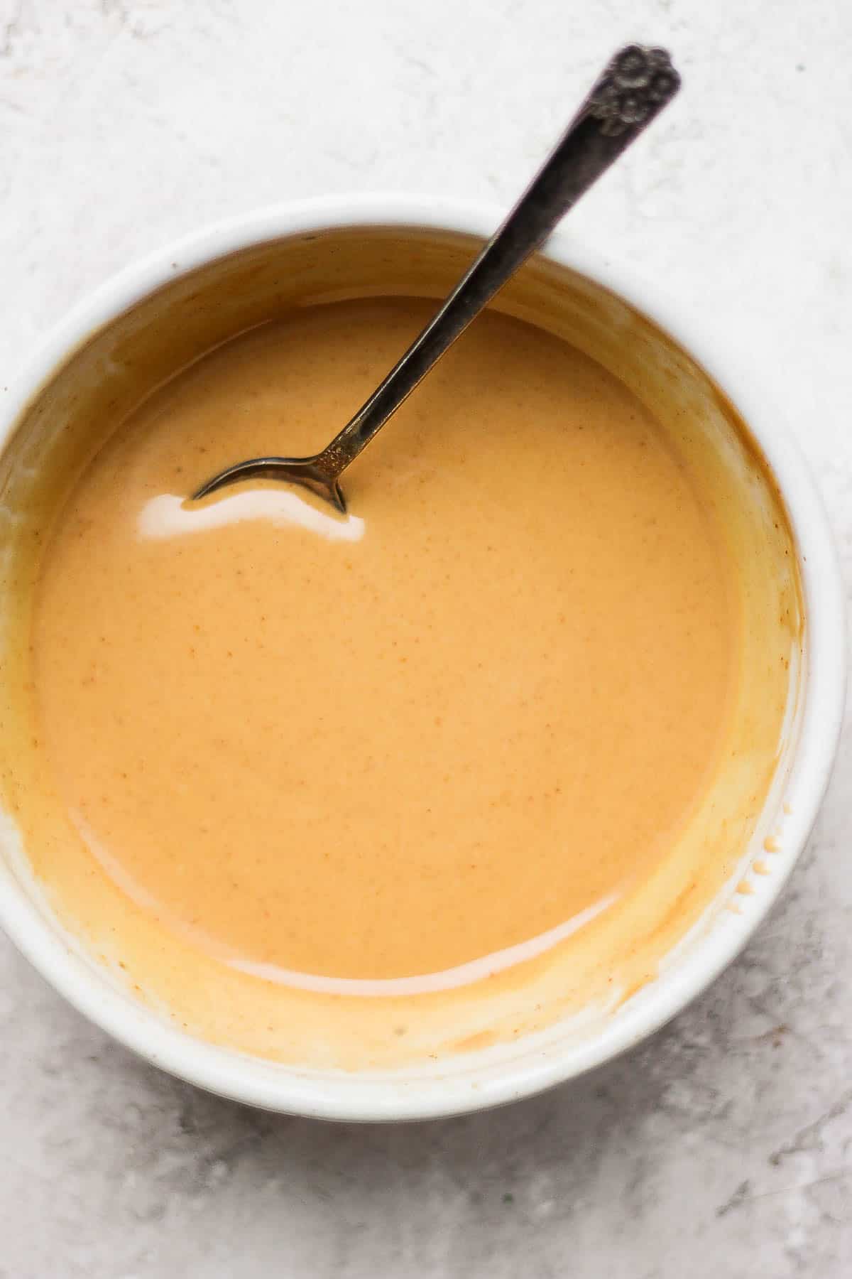 Peanut sauce in a small bowl with a spoon in the sauce leaning on the side of the bowl.