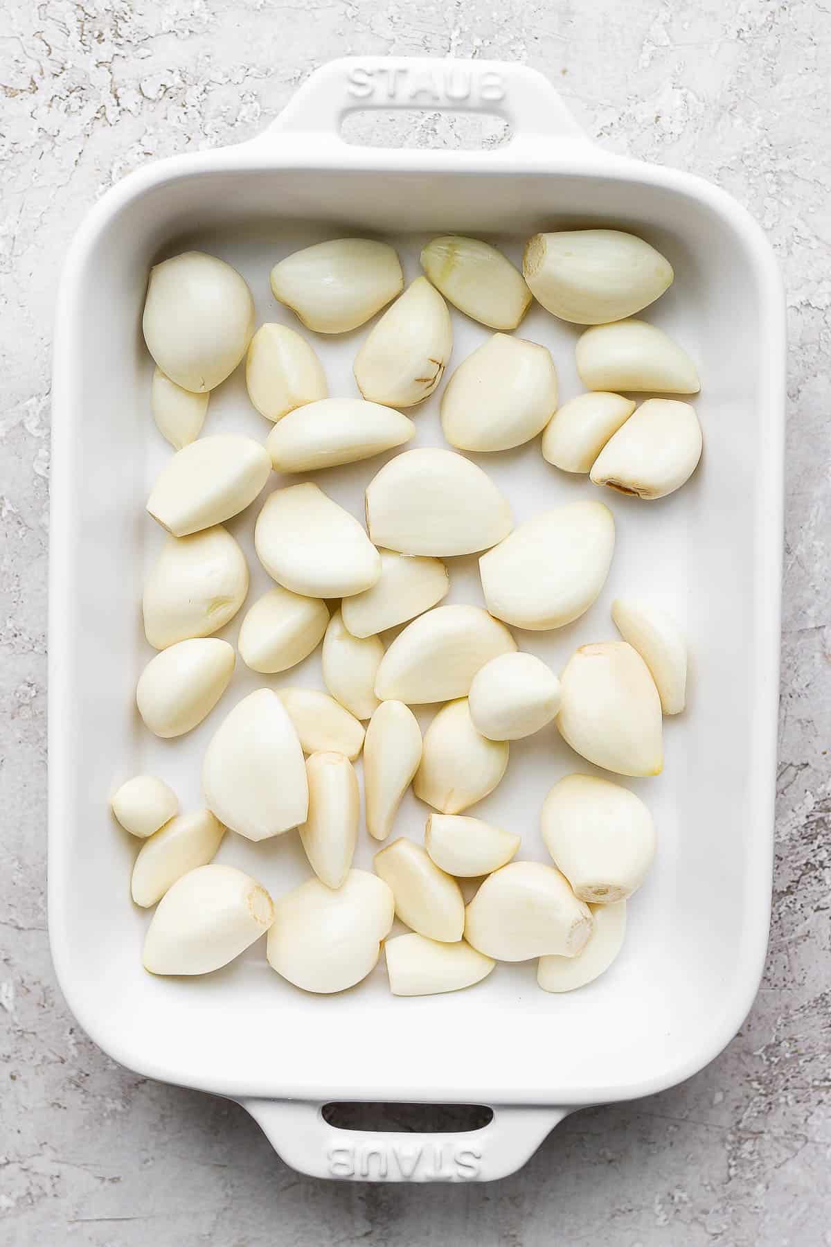 Peeled garlic cloves in a small, shallow baking dish.