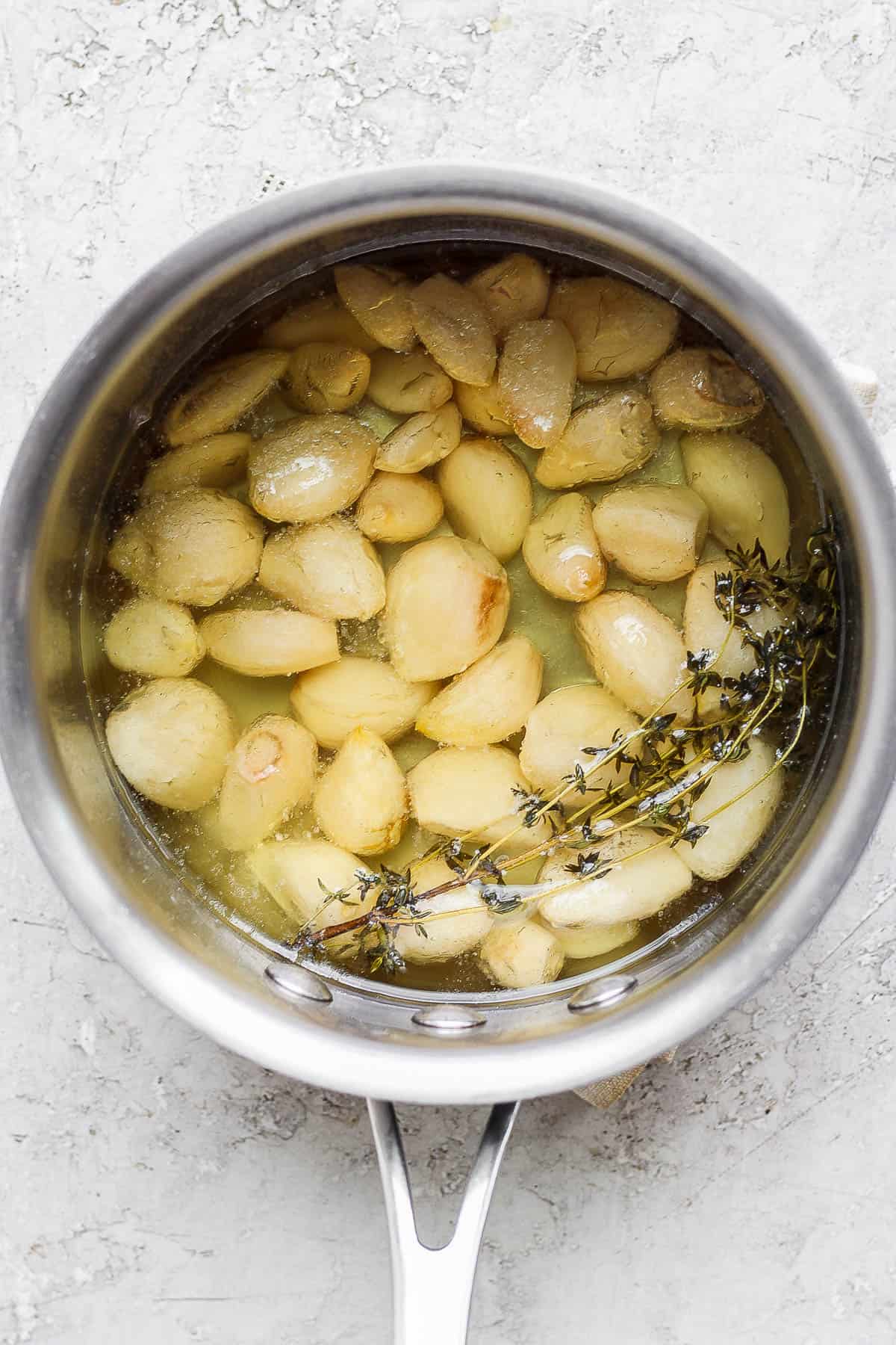 Garlic confit in the saucepan after simmering for 1 hour.