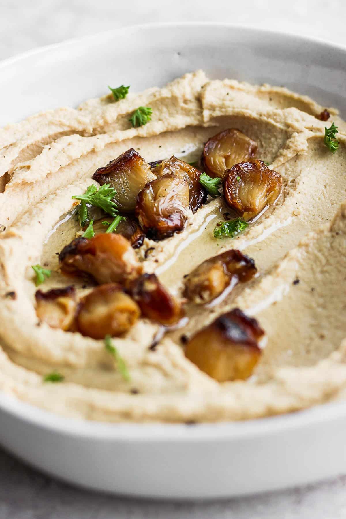 A layer of hummus smoothed out on the bottom of a bowl topped with a few roasted garlic cloves and freshly chopped parsley.