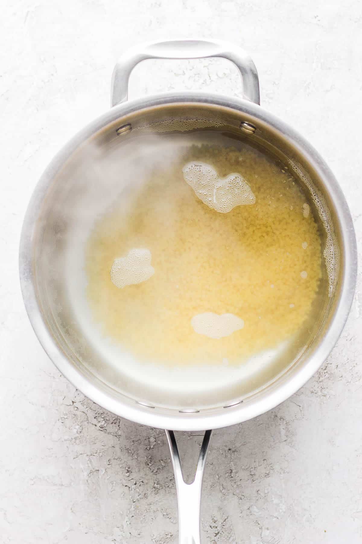 Acini di pepe submerged in a pot of simmering water.