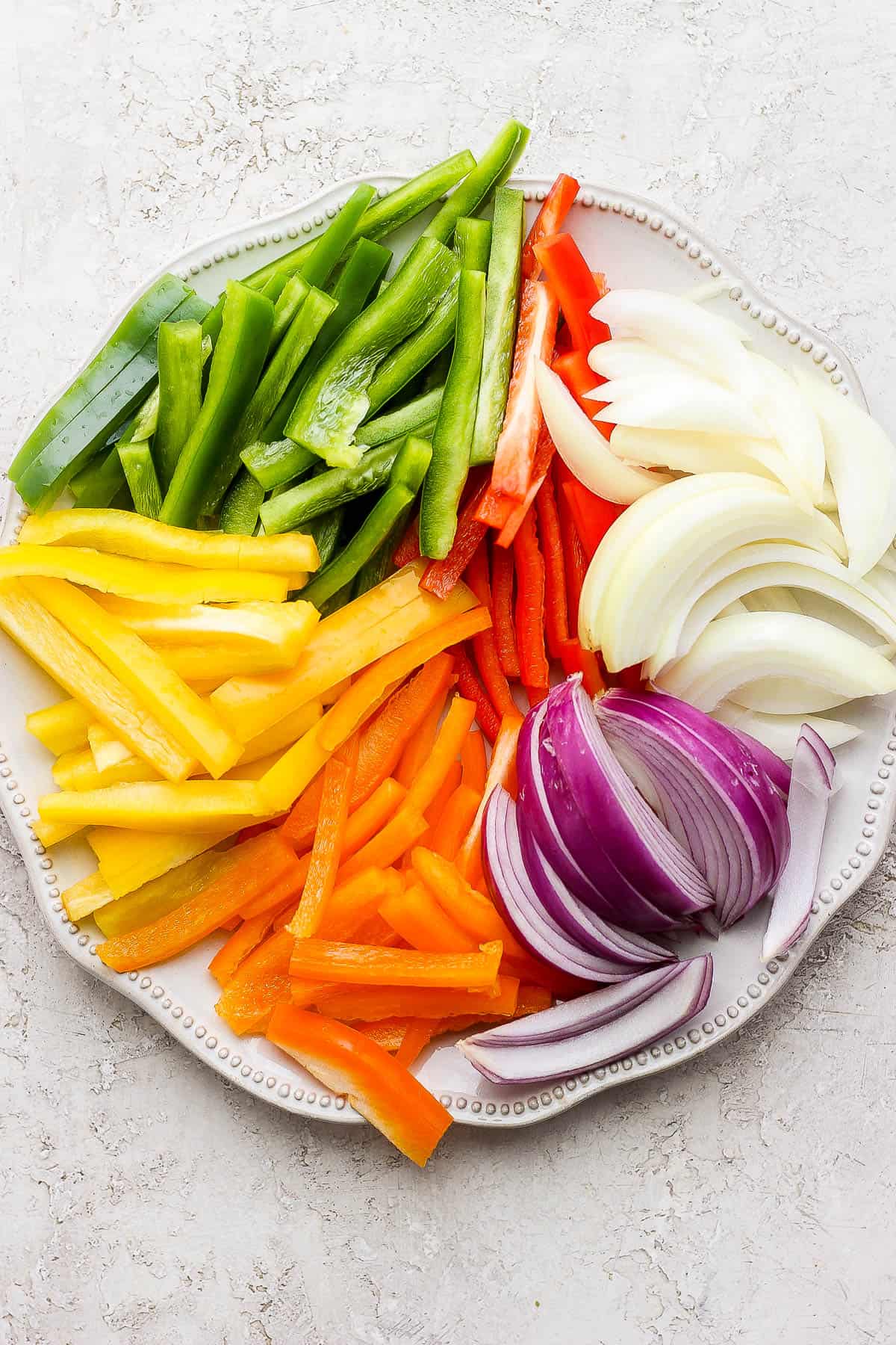 Cut up peppers and onions on a large white plate.