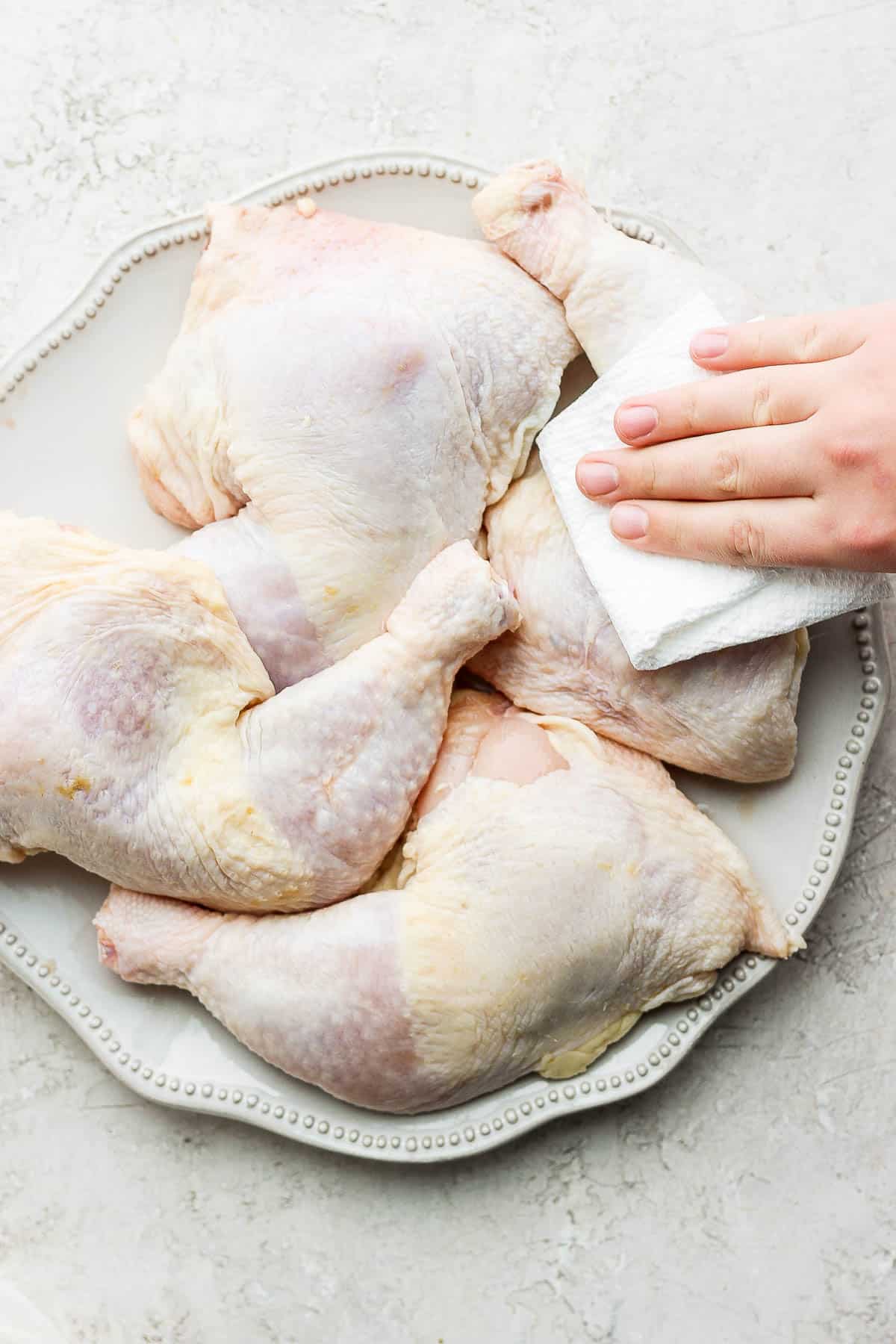 Chicken quarters on a plate being pat dry.