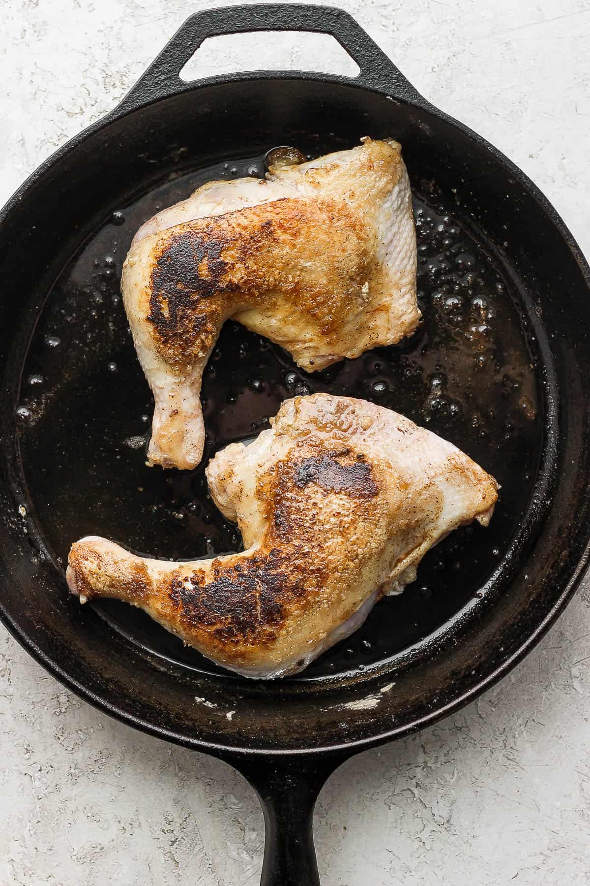 Chicken quarters being seared in a large cast iron skillet.