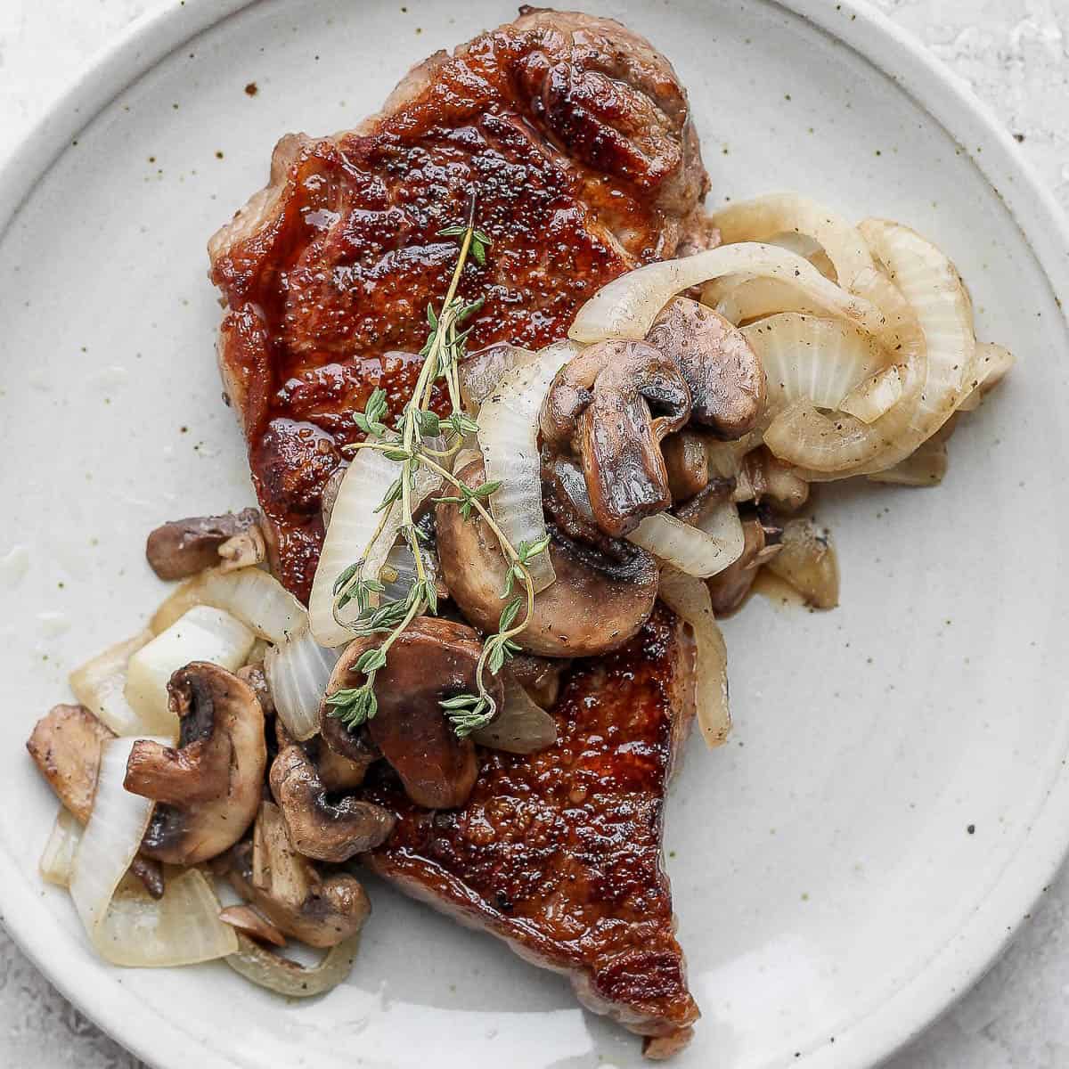 Sautéed mushrooms and onions on a steak on a plate.