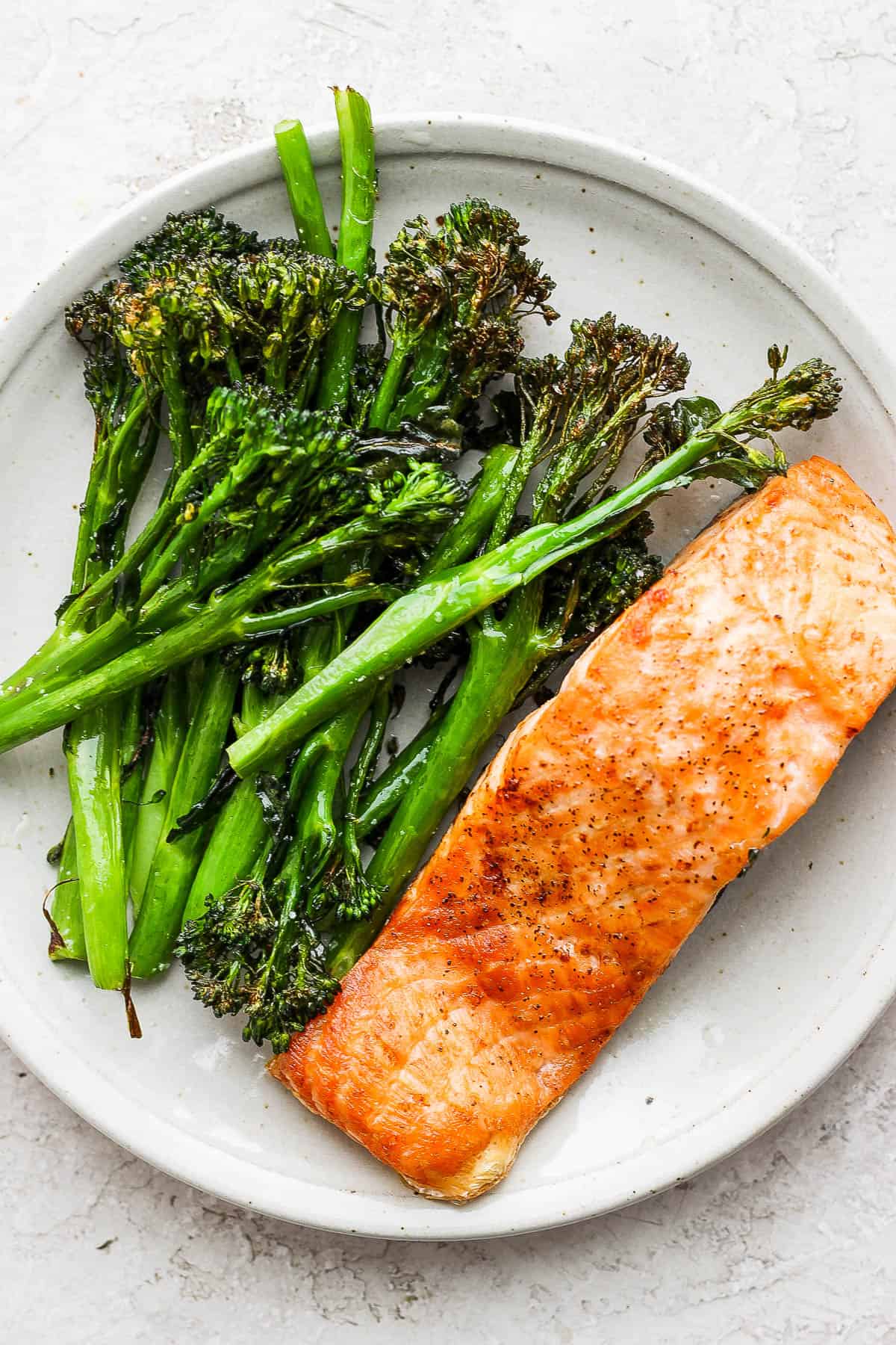 Air fried broccolini on a plate with air fried salmon.