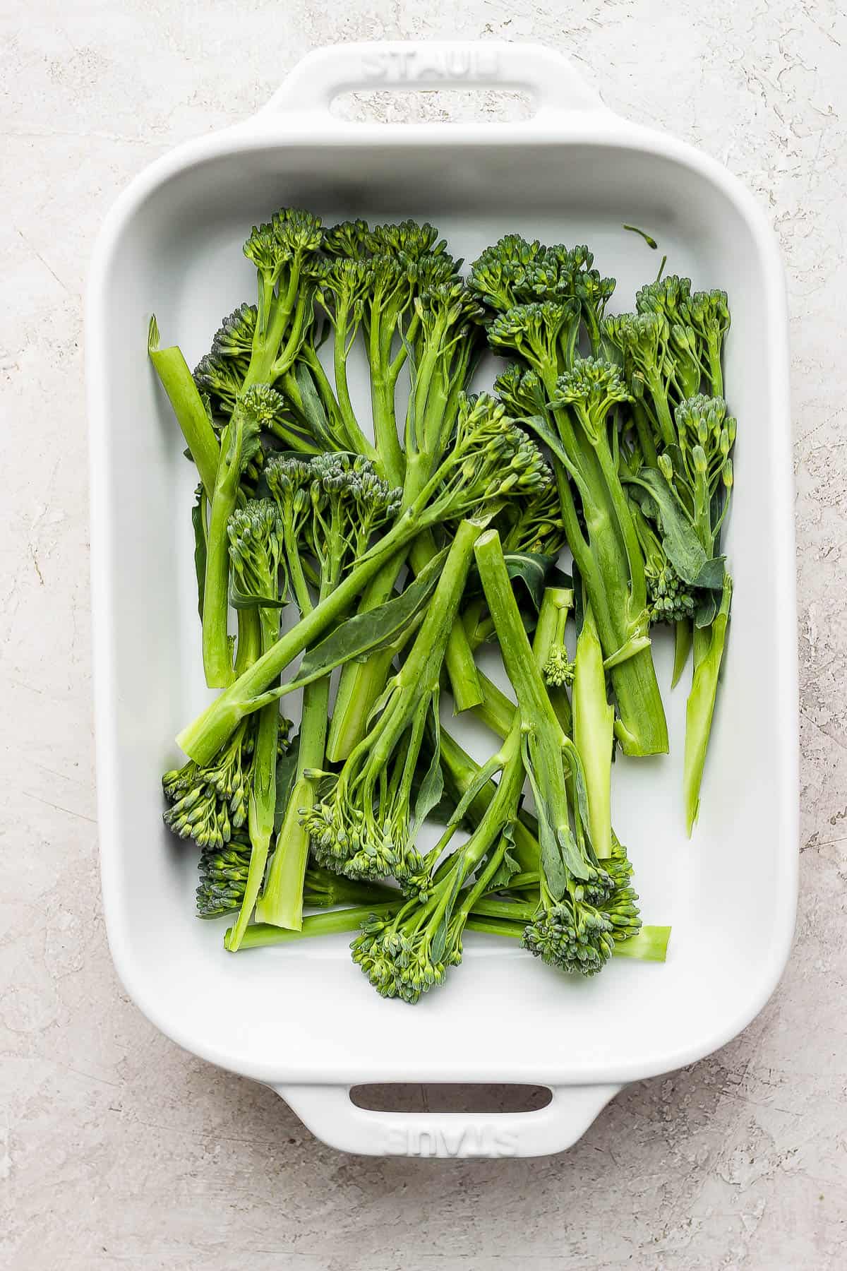 Fresh broccolini with trimmed stems in a shallow baking dish.