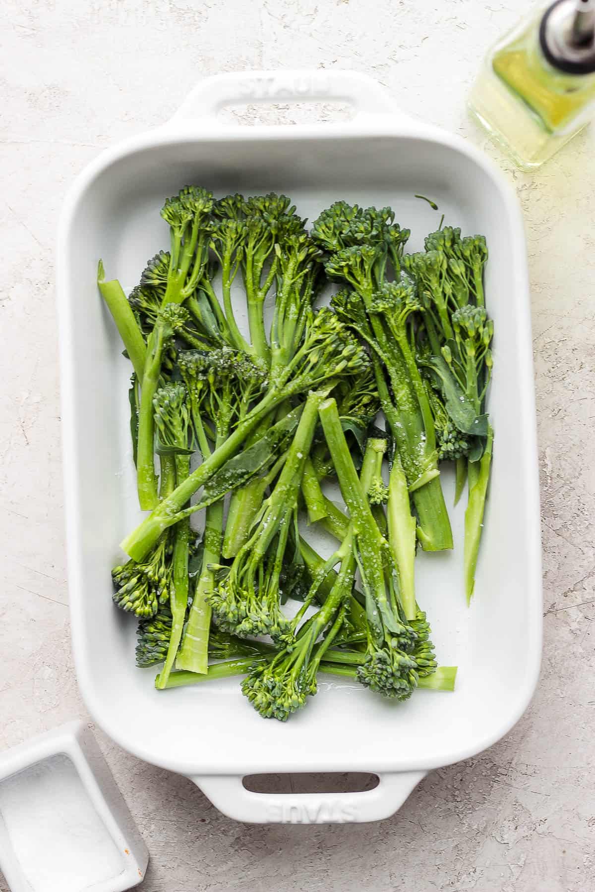 Broccolini in a dish with olive oil and salt on top of it.