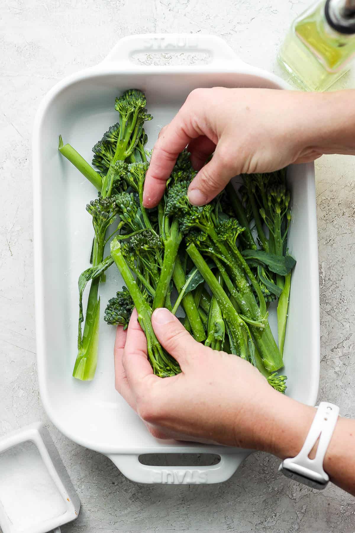 Two hands massaging olive oil and salt on the broccolini.