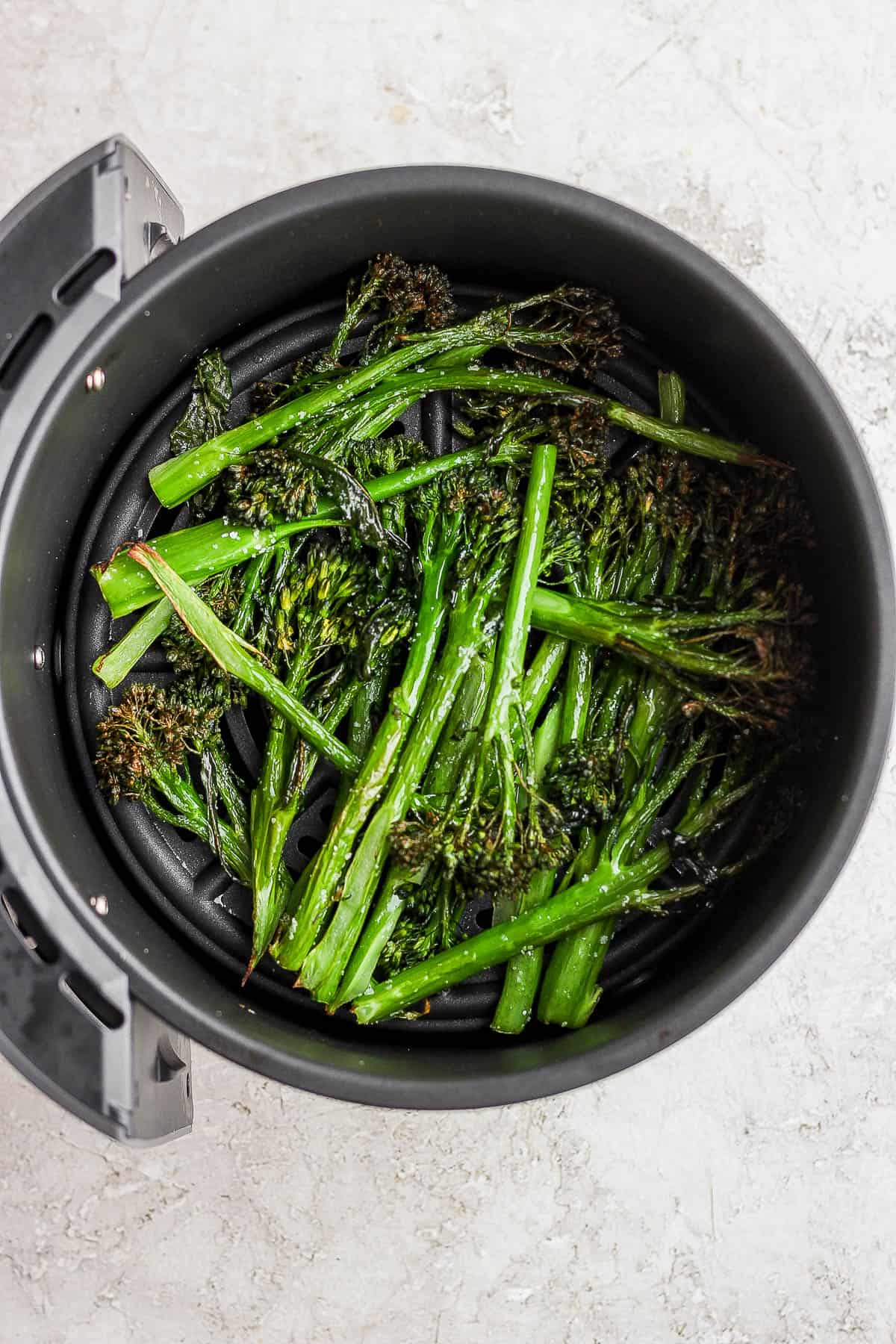 The air fryer basket with broccolini after cooking.