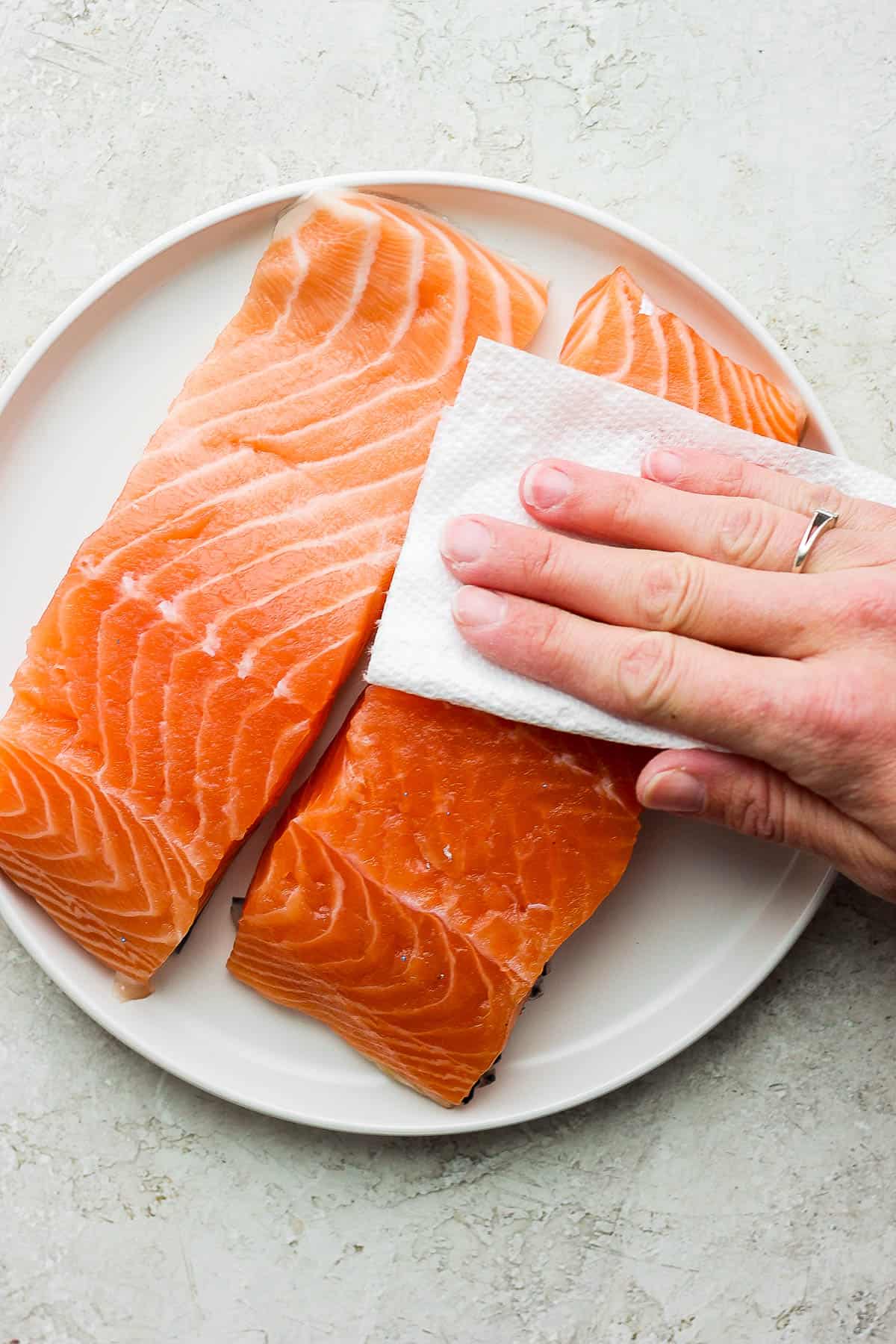 Fresh salmon fillets on a white plate, being pat dry.