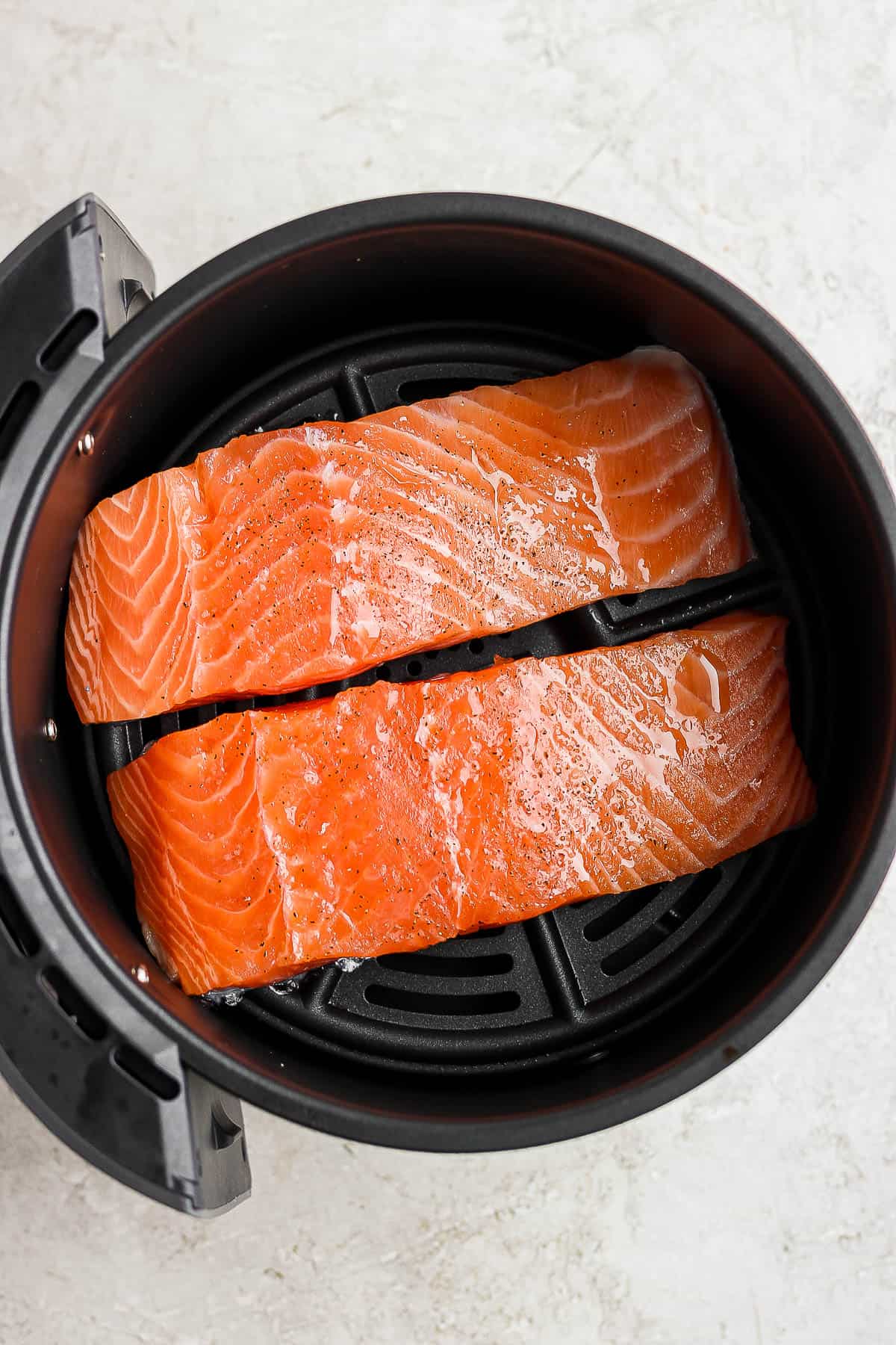 Salmon fillets in an air fryer basket before cooking.
