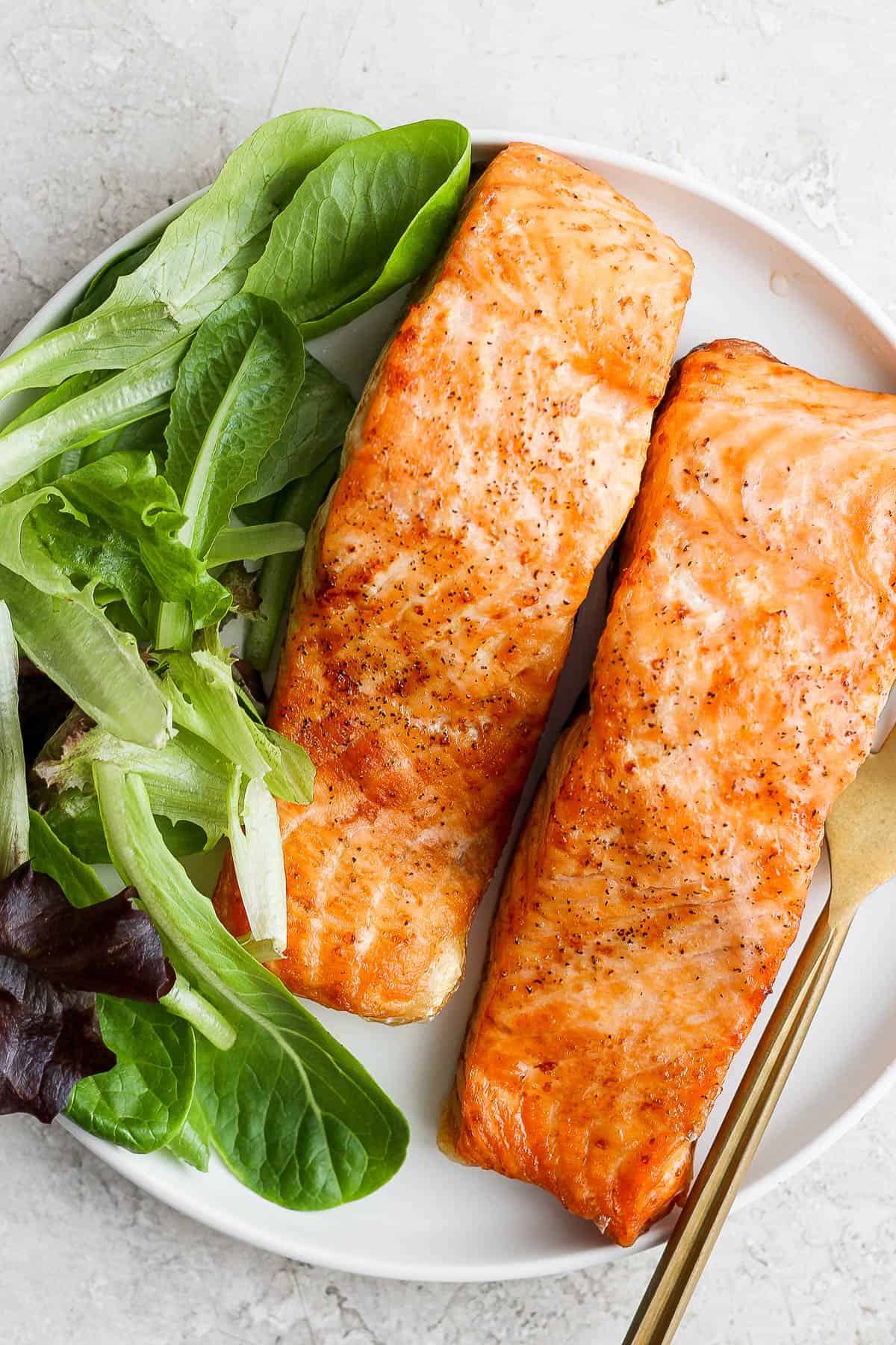 Air fried salmon fillets on a white plate with a side salad.