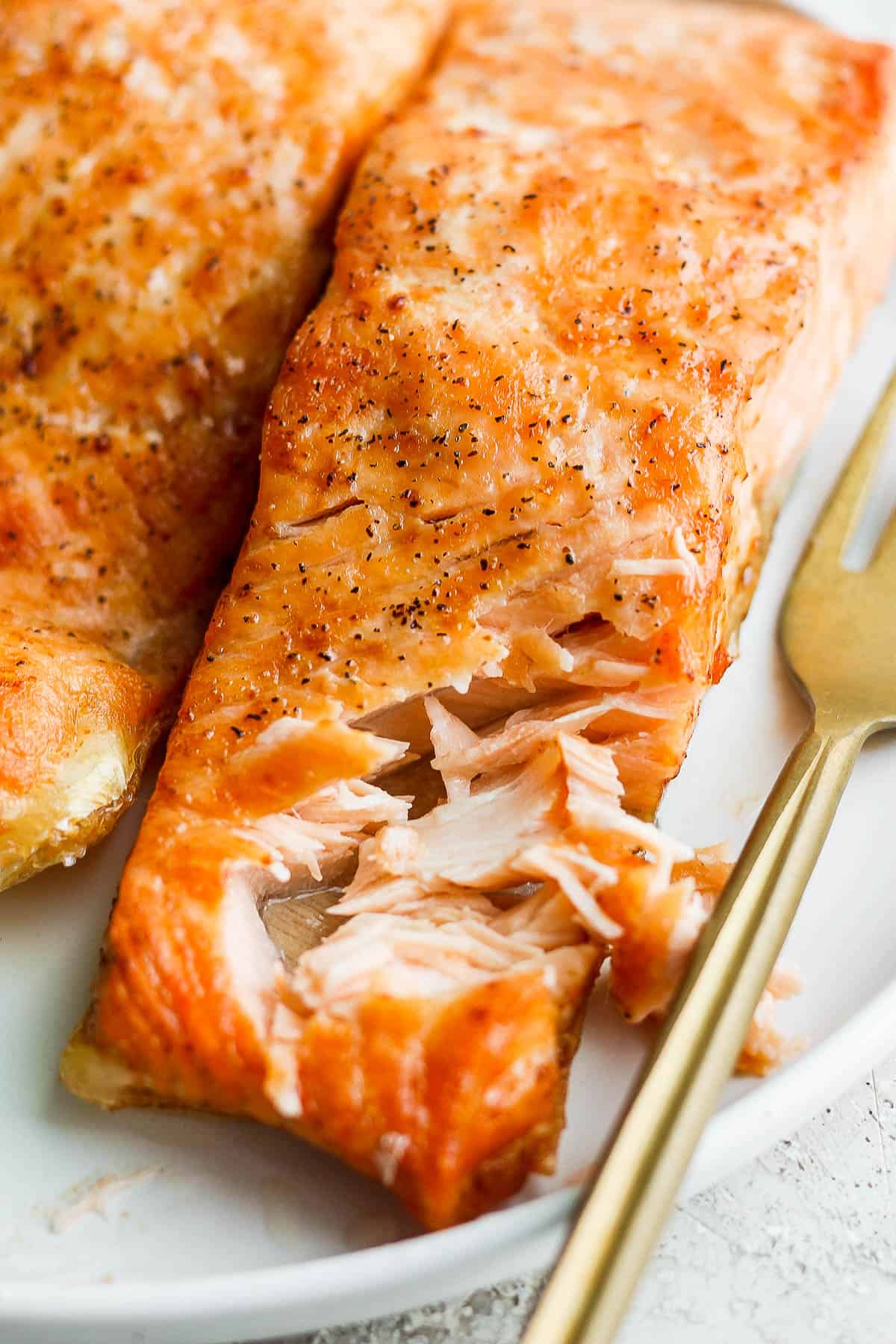 Part of one salmon fillet flaked apart with a fork.