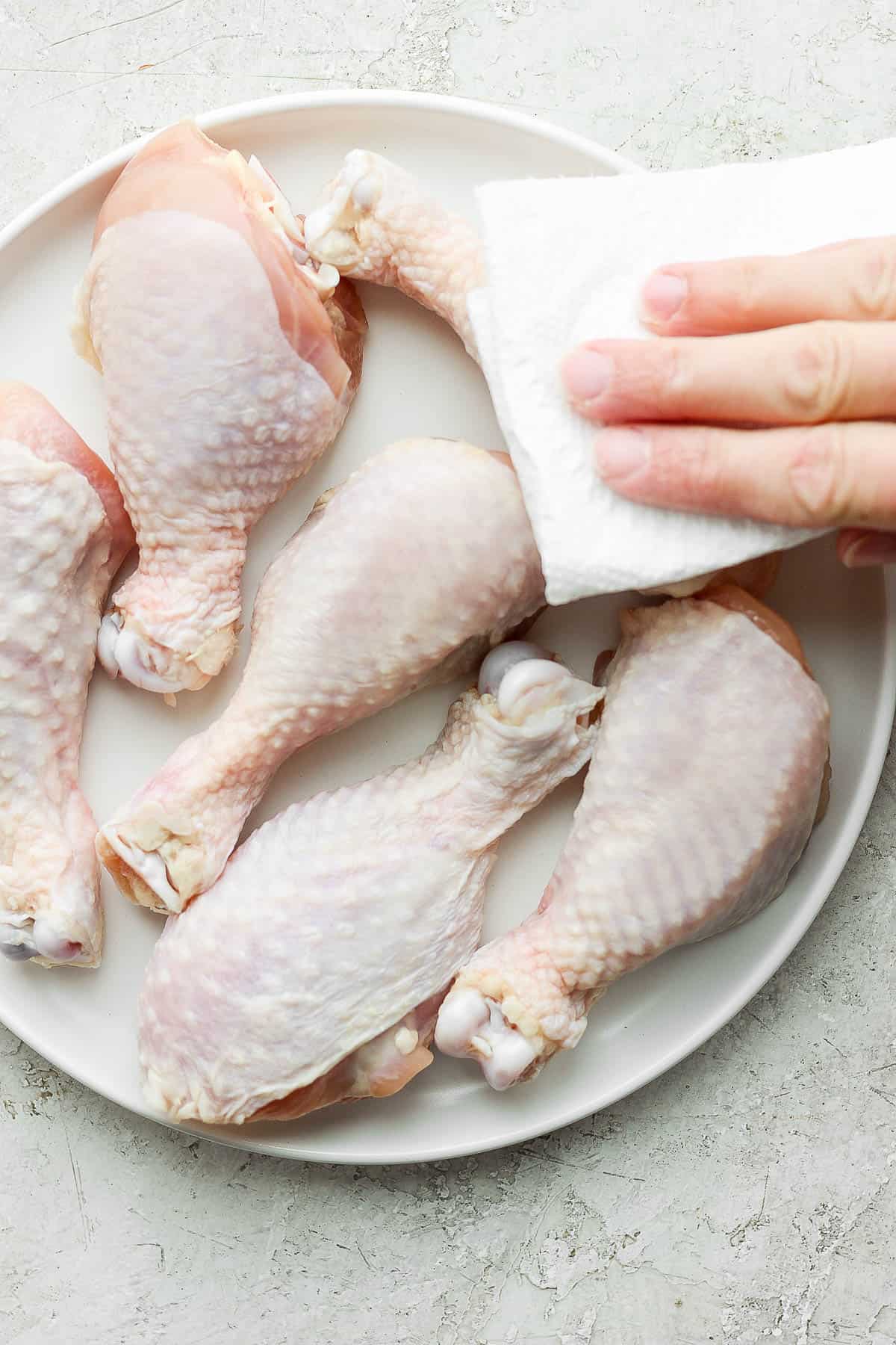Raw chicken legs on a white plate being pat dry.