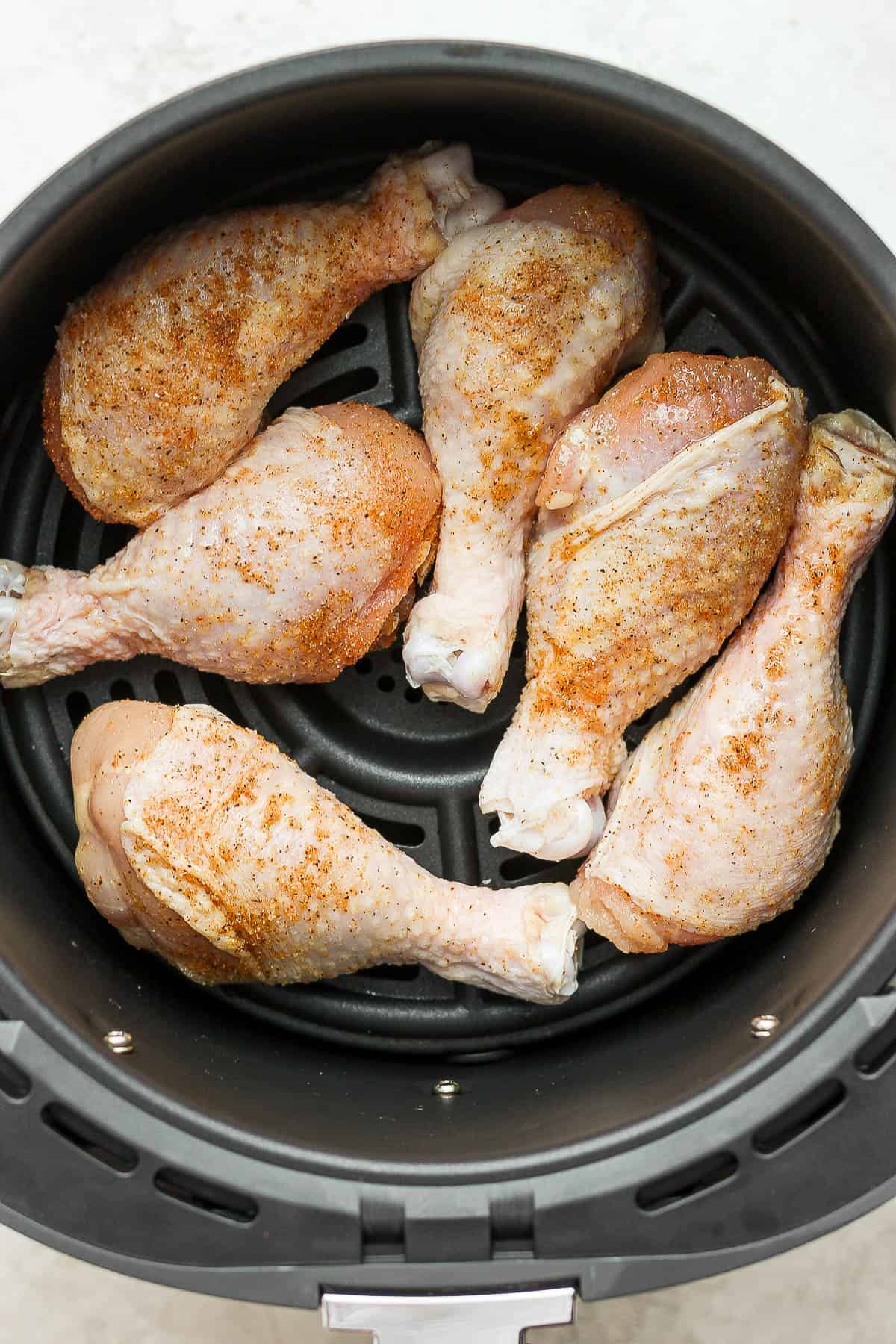 Seasoned chicken legs in the air fryer basket before cooking.