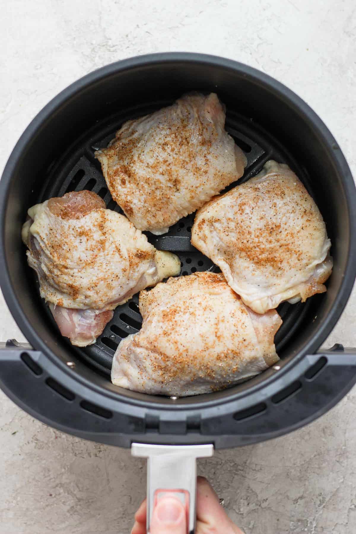 Seasoned chicken thighs in the air fryer basket before being cooked.