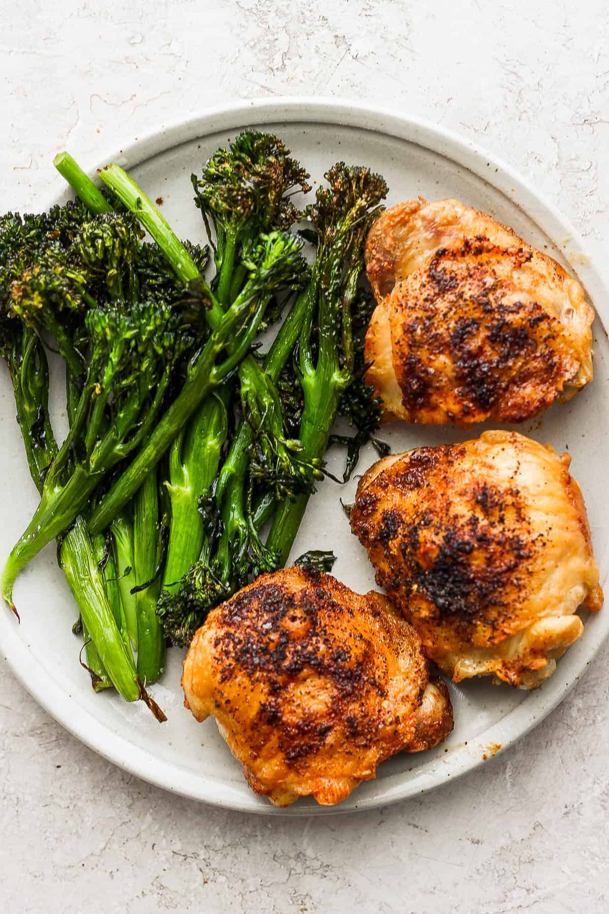 Air fried chicken thighs on a plate with air fried broccolini.