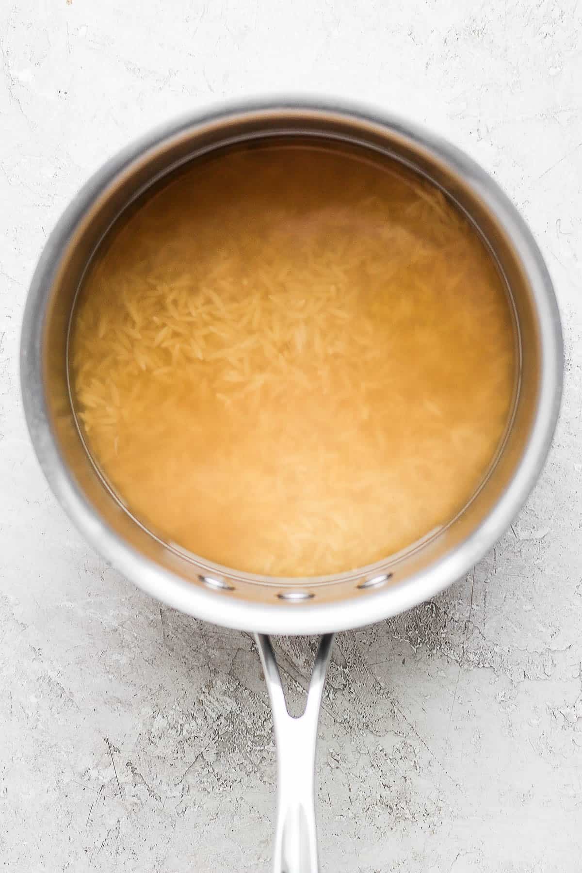 Orzo cooking in a pot with chicken broth and water.