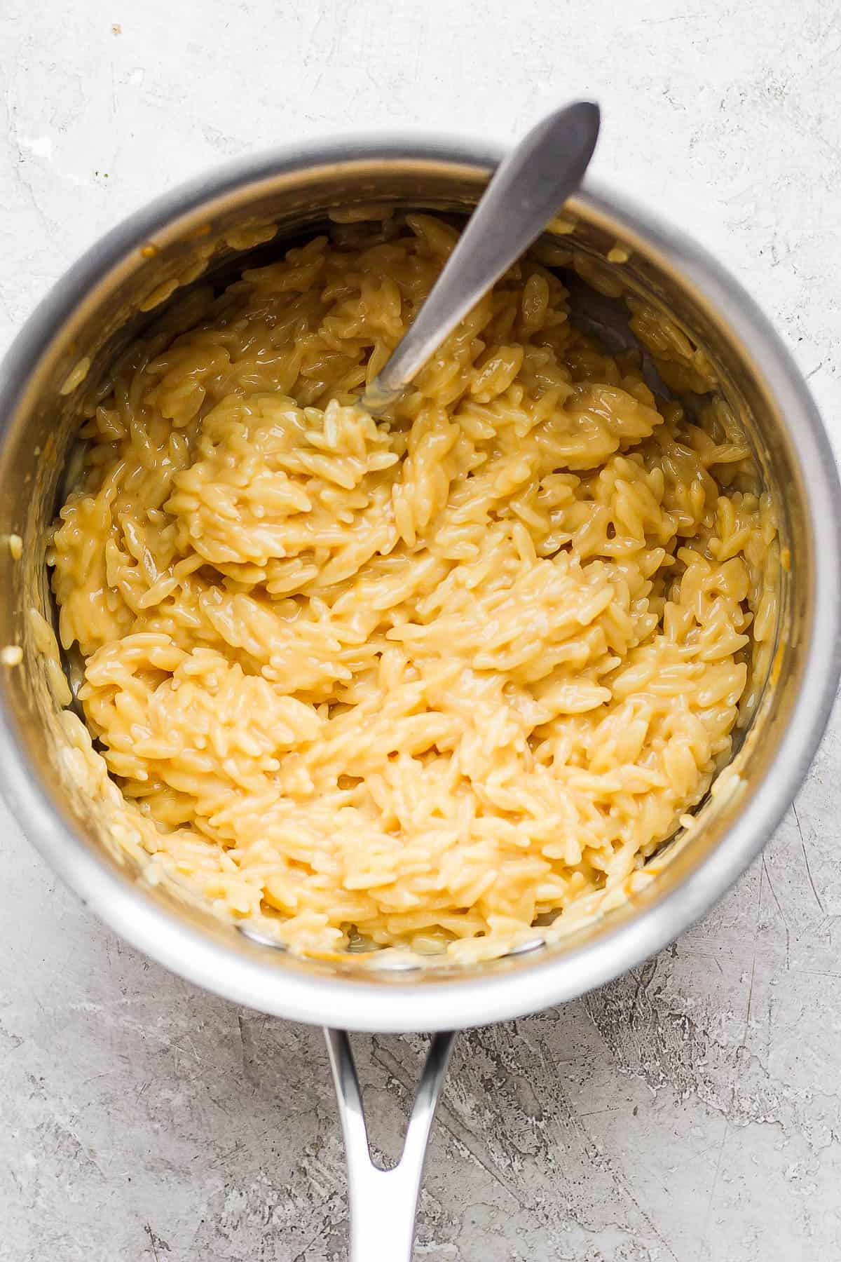 Cheesy orzo in a pot with a spoon.
