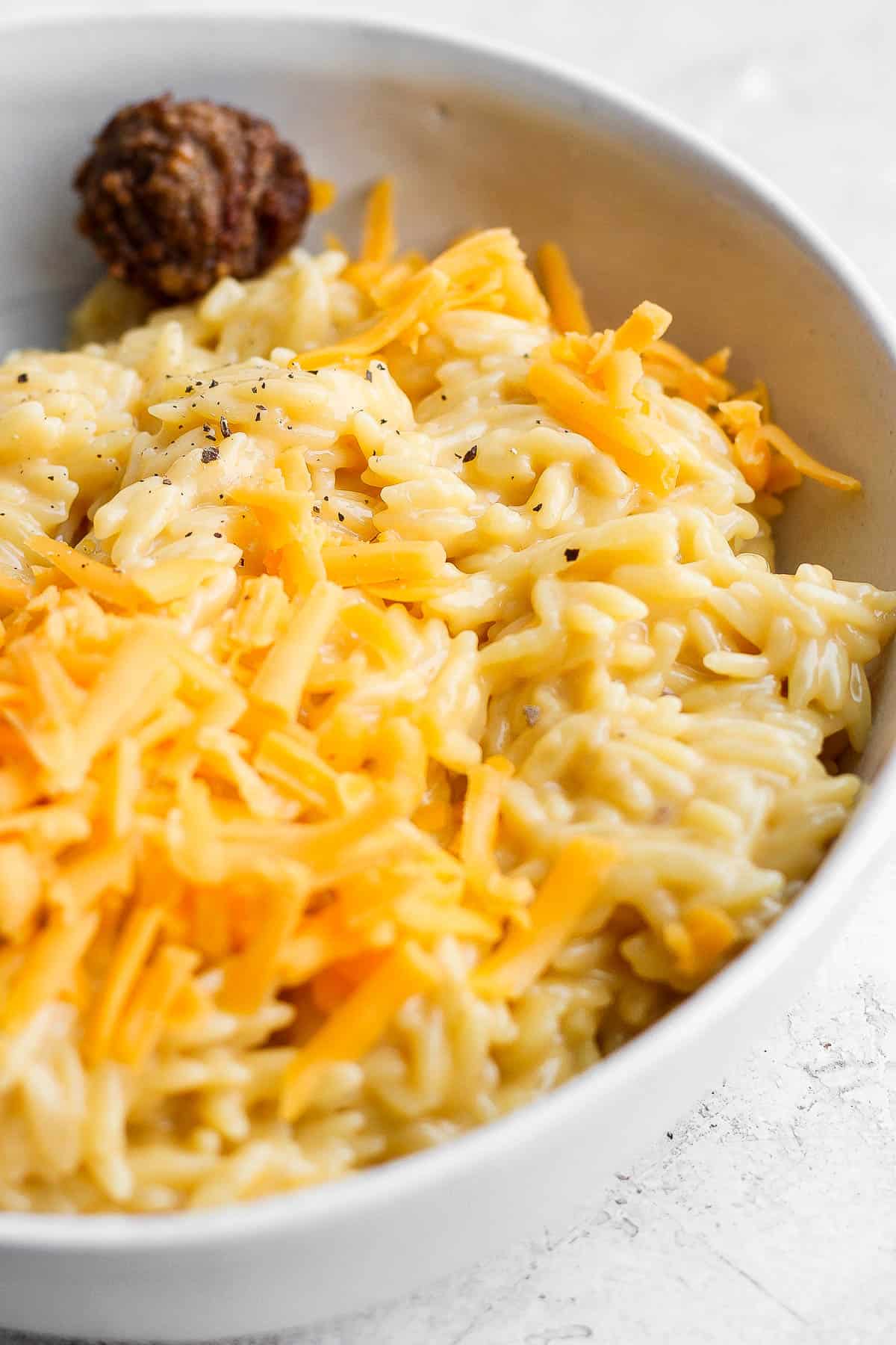 Cheesy orzo in a white bowl with salt and pepper sprinkled on top.