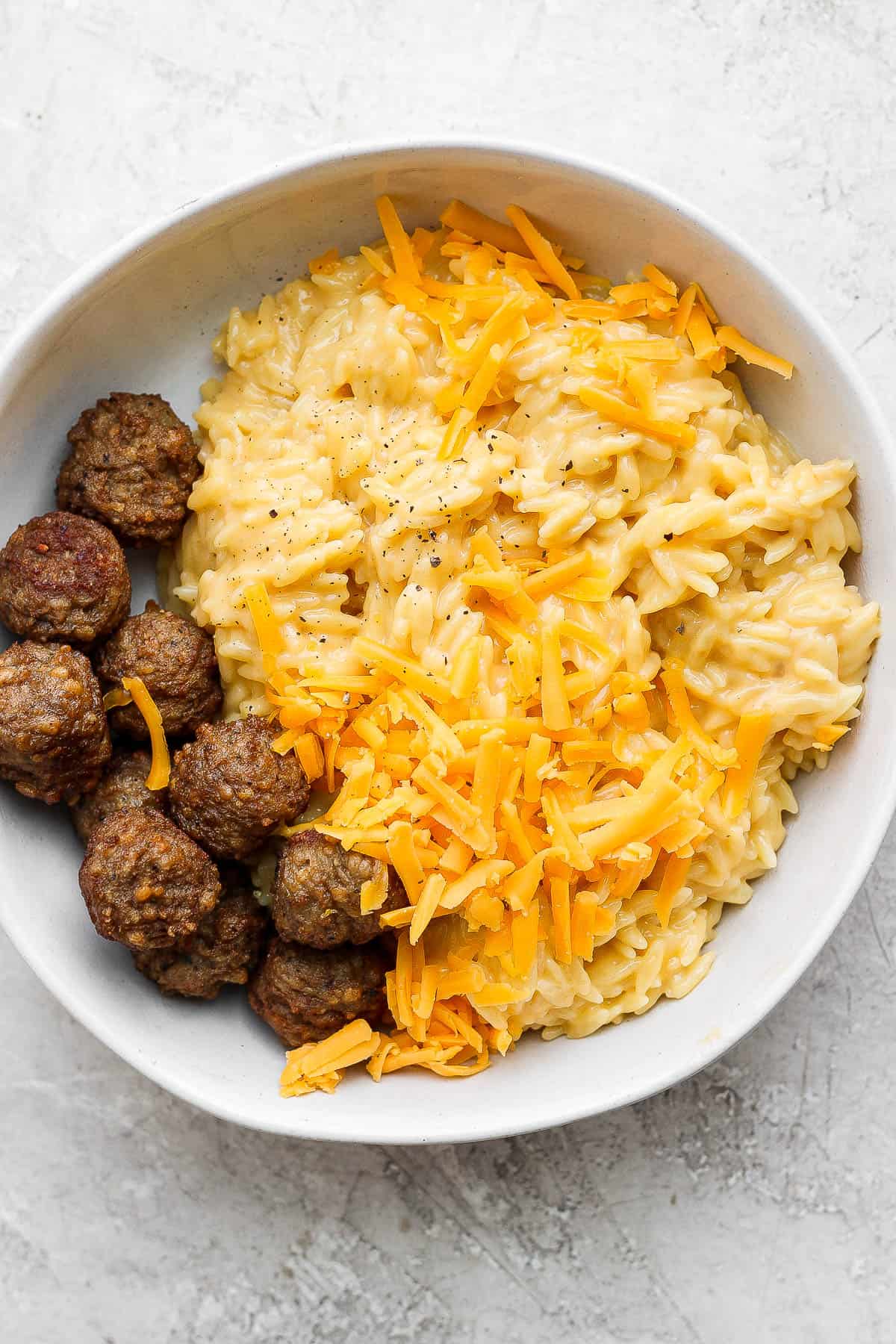 Cheesy orzo in a white bowl with meatballs.