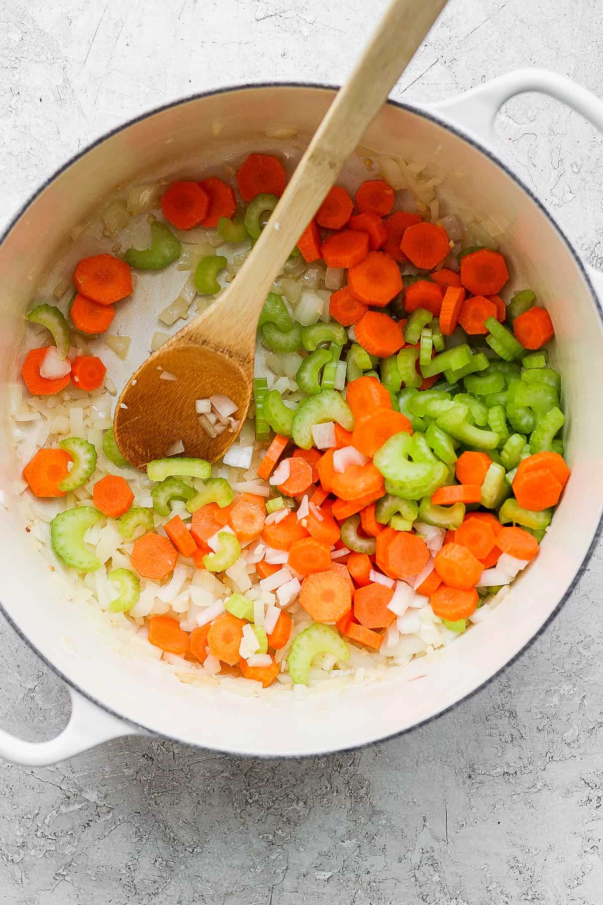 minced garlic, chopped onion, sliced celery, and chopped carrot sauteing in a large dutch oven with a wooden spoon for stirring.