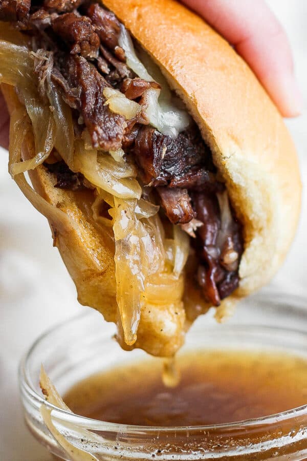 Someone dipping a French Dip sandwich into a little bowl of au jus.