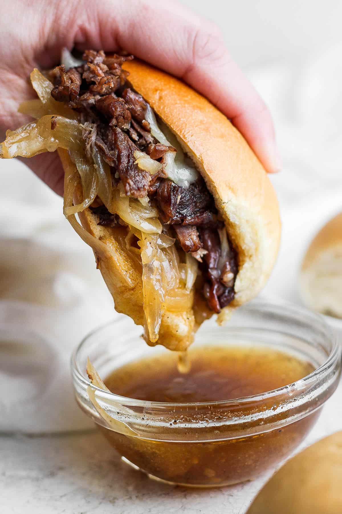 A french dip sandwich being dipped in the au jus.