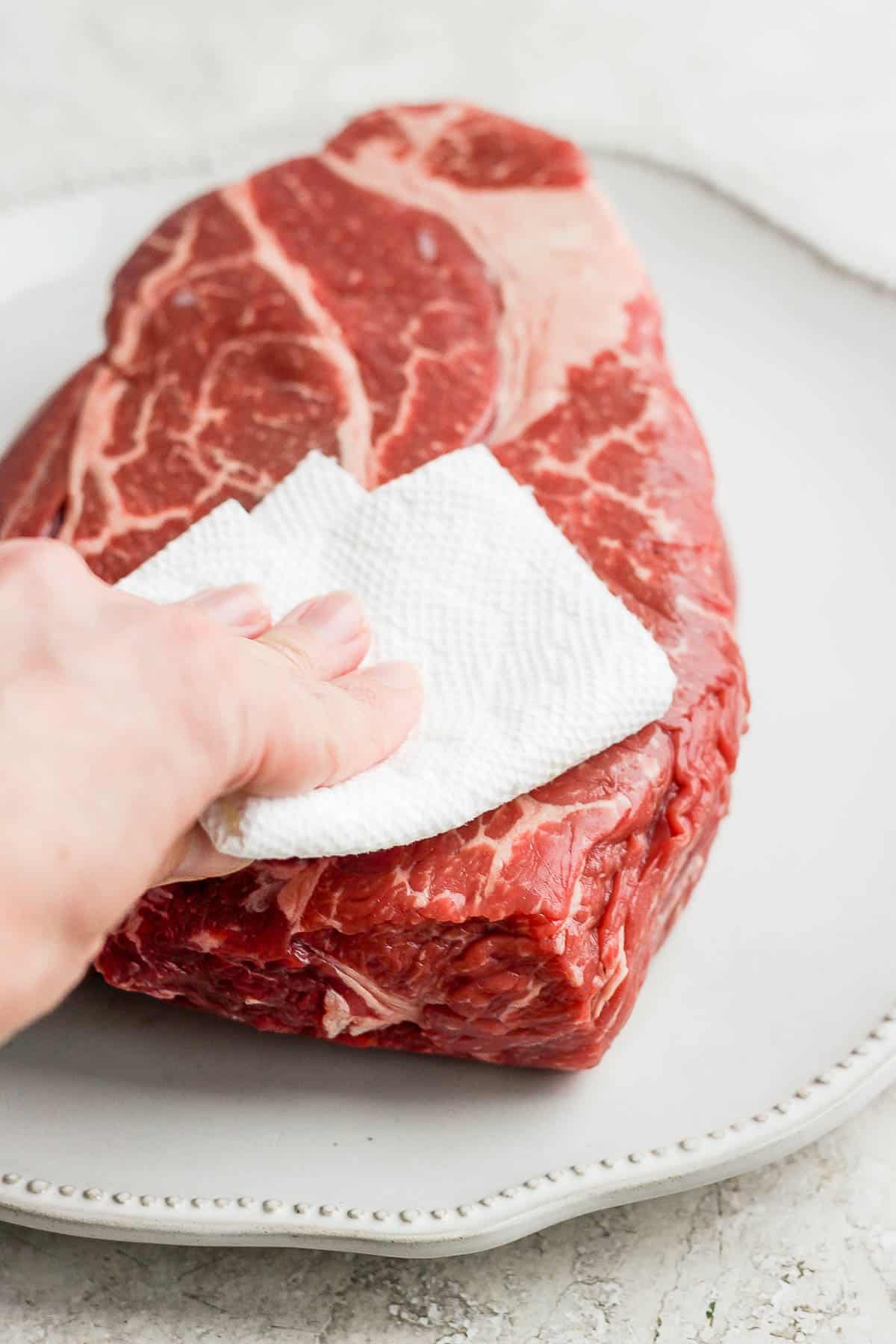 A chuck roast being pat dry on a white plate.