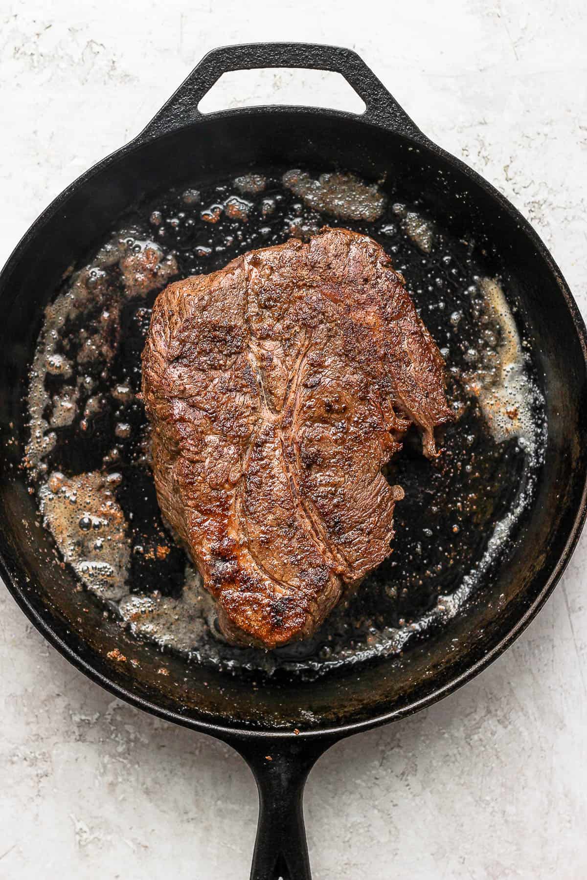 The seasoned chuck roast being seared in a large cast iron skillet.