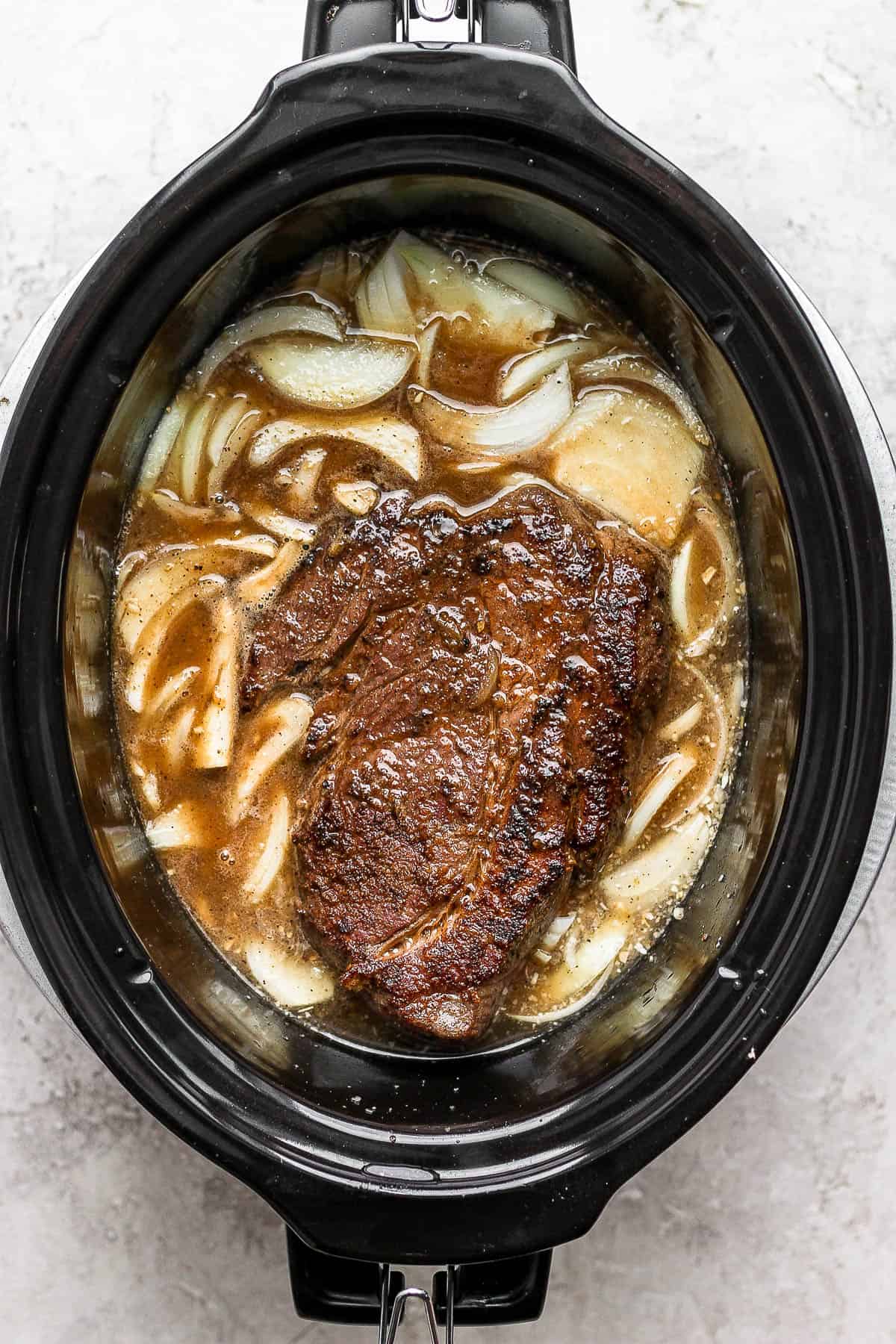 The seared chuck roast in the crockpot with the beef broth mixture.
