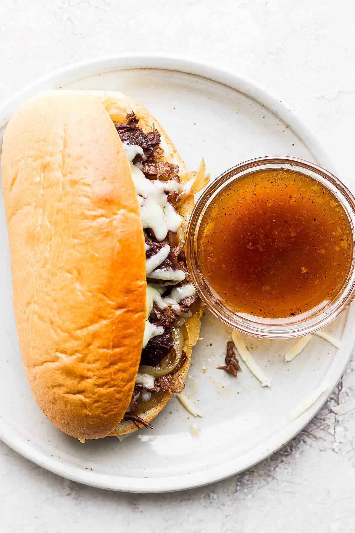 A french dip sandwich on a white plate with a small dish of au jus.