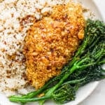 A piece of hot honey chicken in a shallow bowl with brown rice and broccolini.