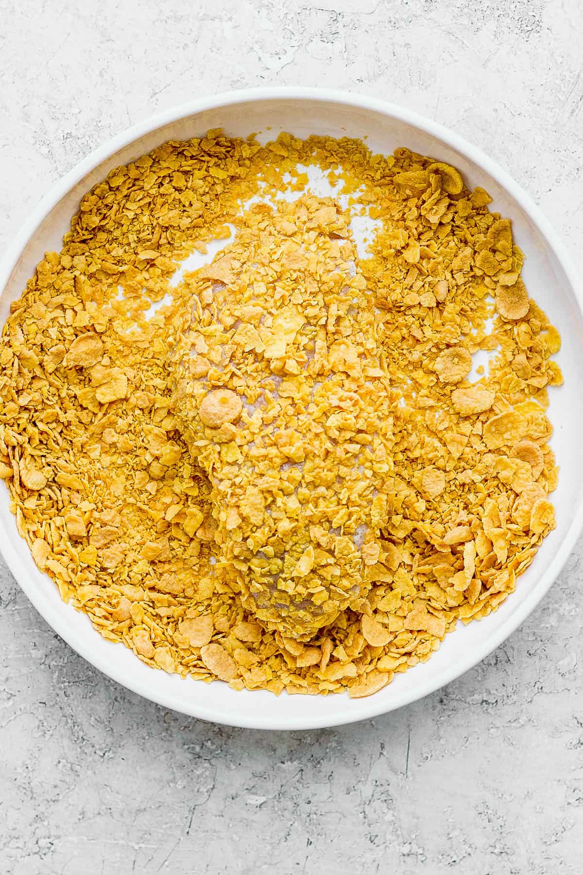 Chicken breast in a bowl with crushed cornflakes.