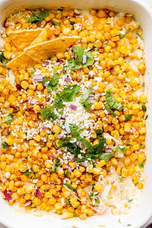 Pan of Mexican Street Corn Dip with a few chips sticking out and garnished with fresh cilantro and chopped cilantro.